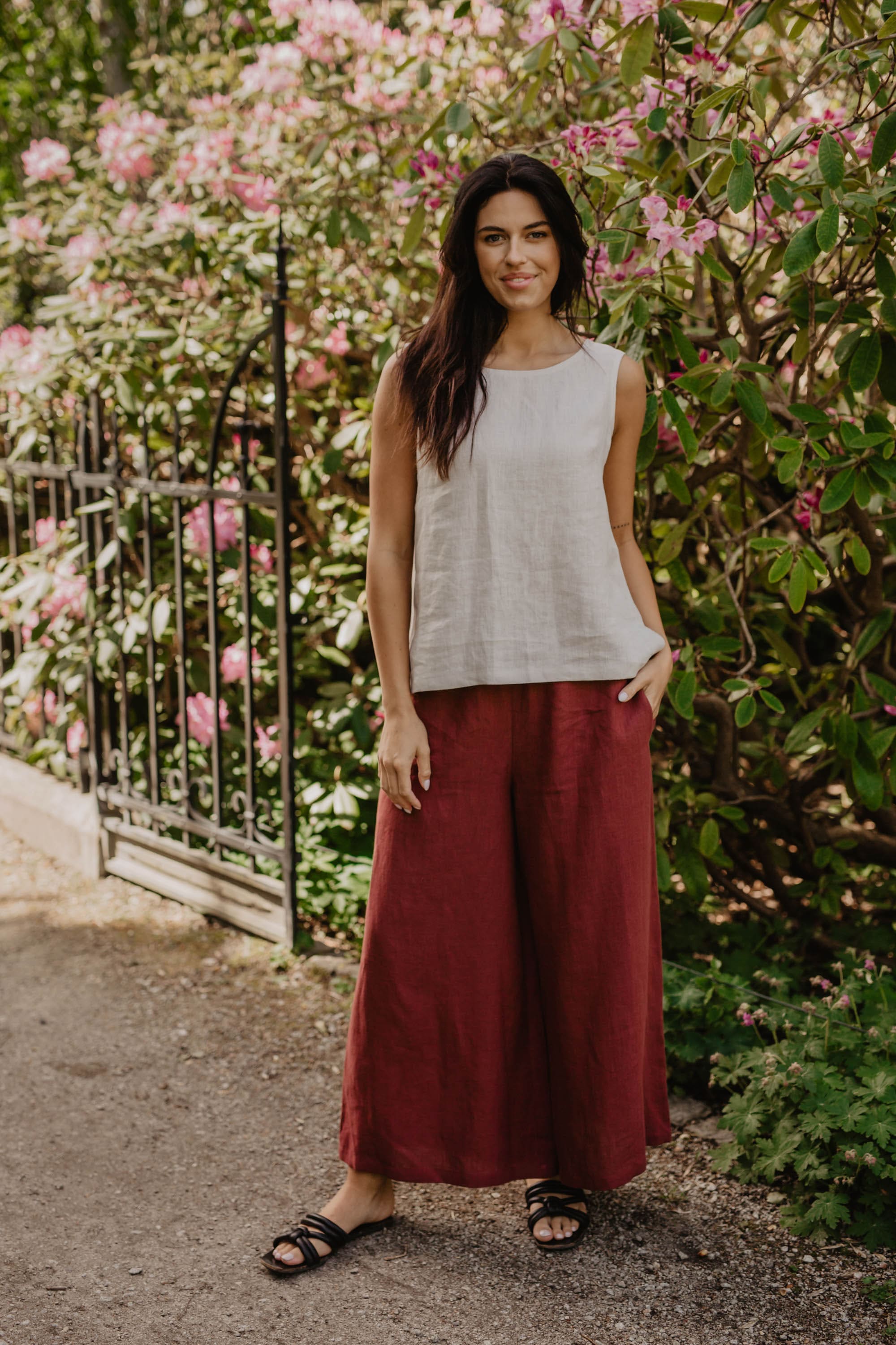 Woman In Flower Garden Facing Forward Wearing A White Linen Top and Red Linen Pants