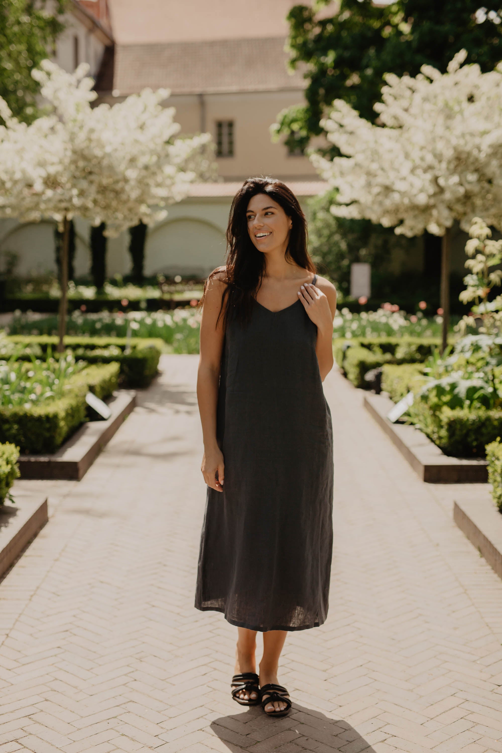 Woman Wearing A Long Dark Linen Dress By AmourLinen In A Blossoming Park