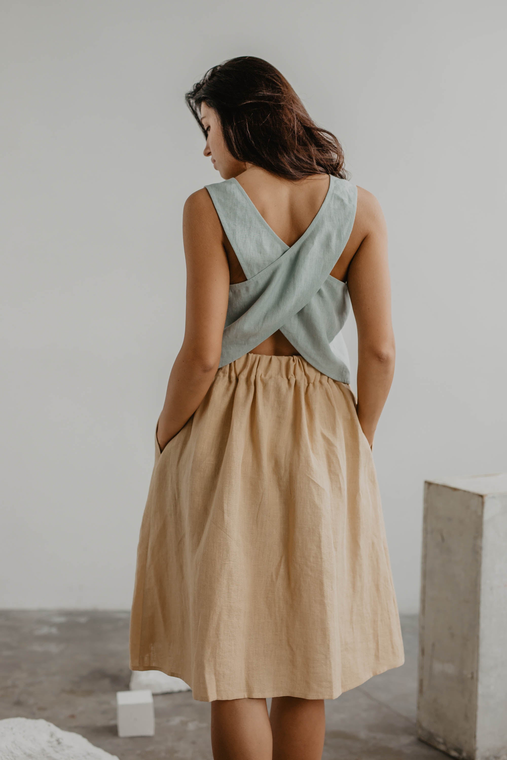 Back Of Woman Wearing A Linen Beige Skirt With Buttons And Sage Green Top By AmourLinen