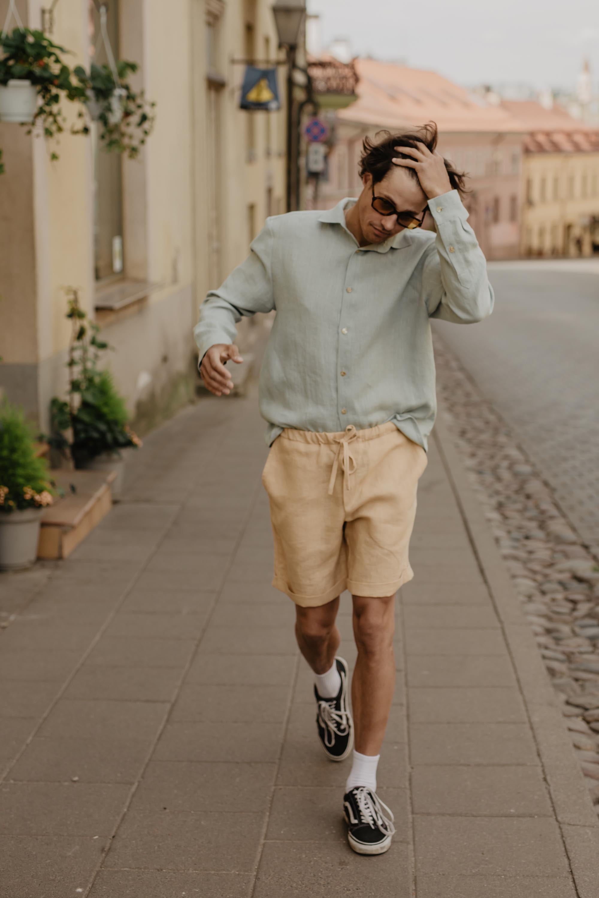 Man Walking Up A Street Wearing Mustard Linen Shorts And Sage Green Shirt