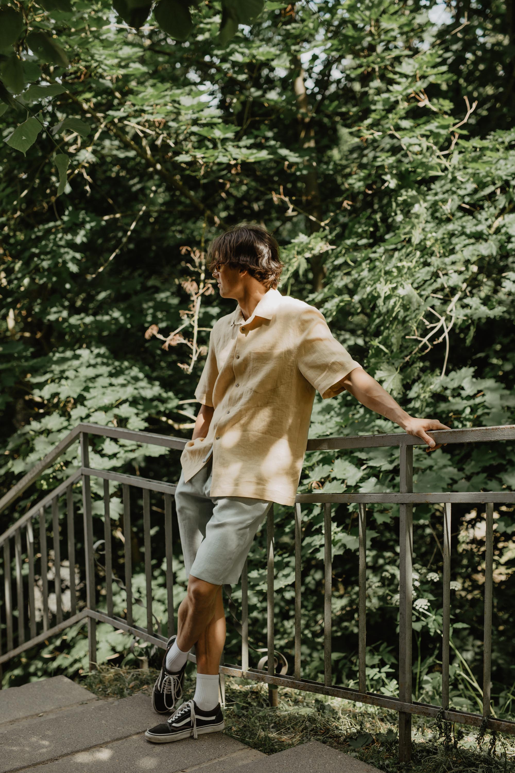 Man Leaning Against Railing Wearing Oversized Mustard Linen Shirt and Sage Green Shorts