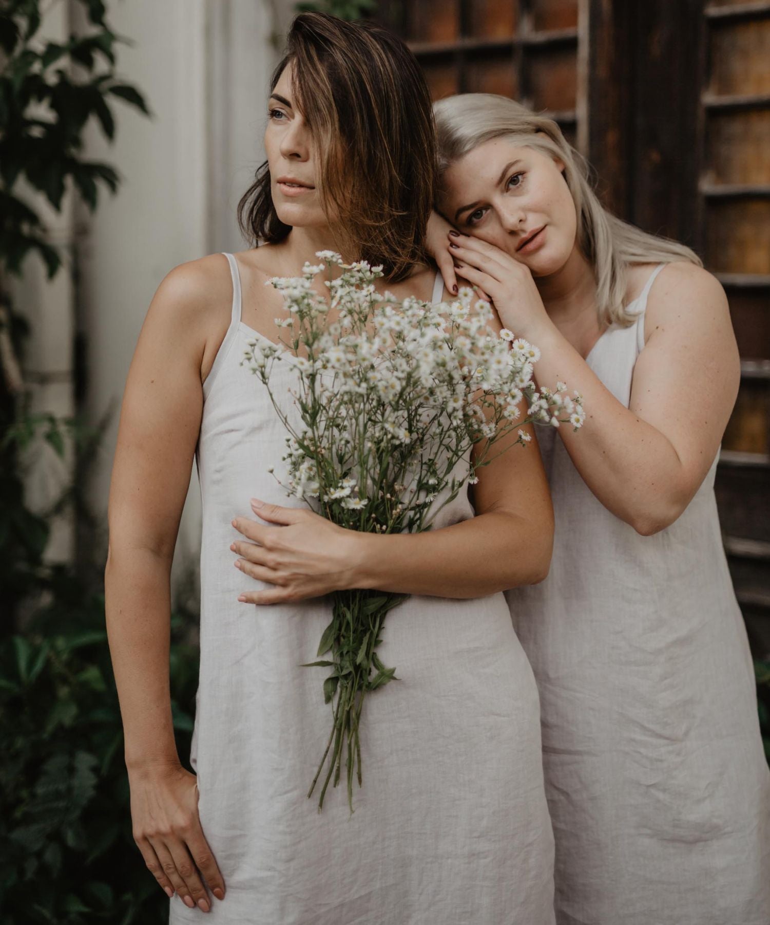 Two Women Standing In Linen Dresses With A Bouquet Of Flowers