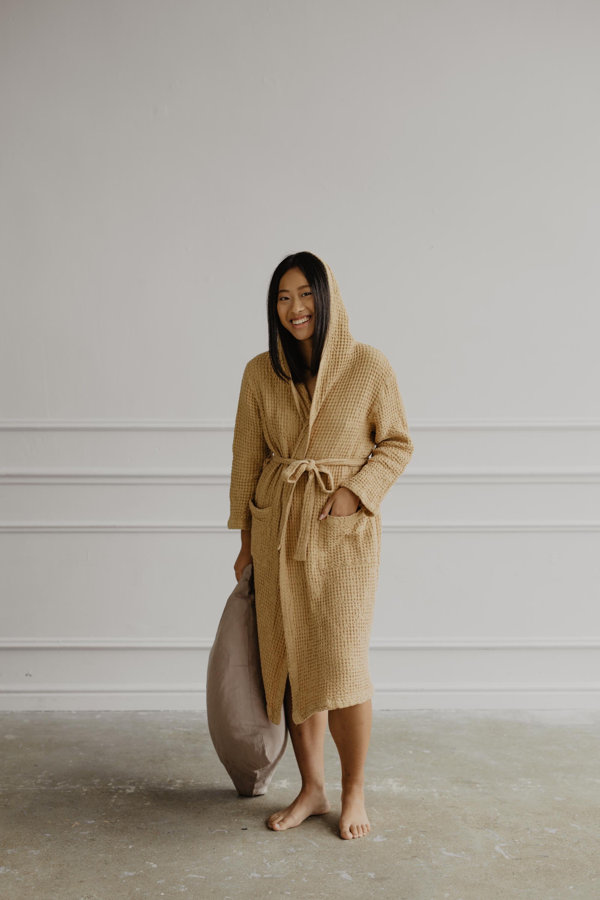 Woman Holding A Pillow And Wearing A Mustard Color Linen Waffle Bathrobe