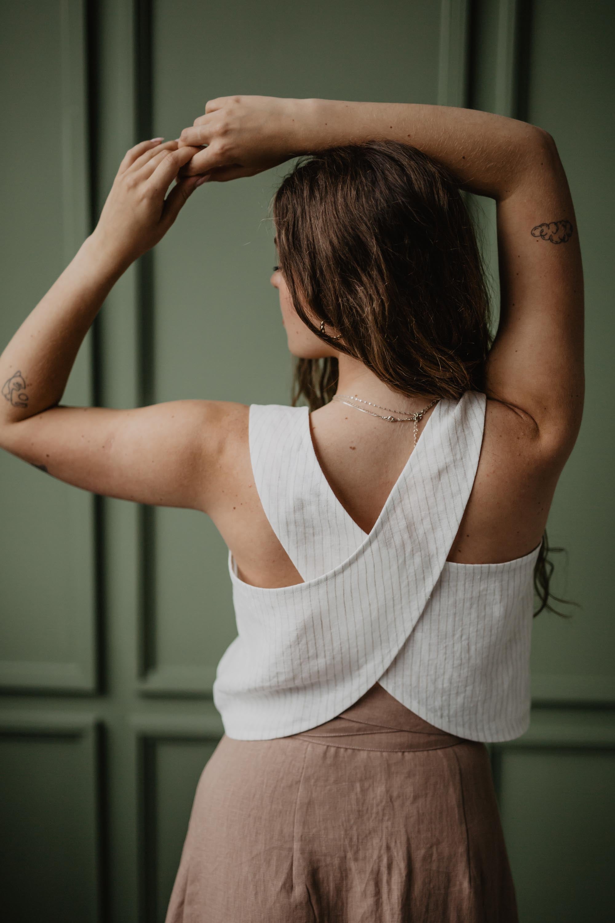 Back OF woman Wearing A White Linen Pinafore Top In A Dark Green Room