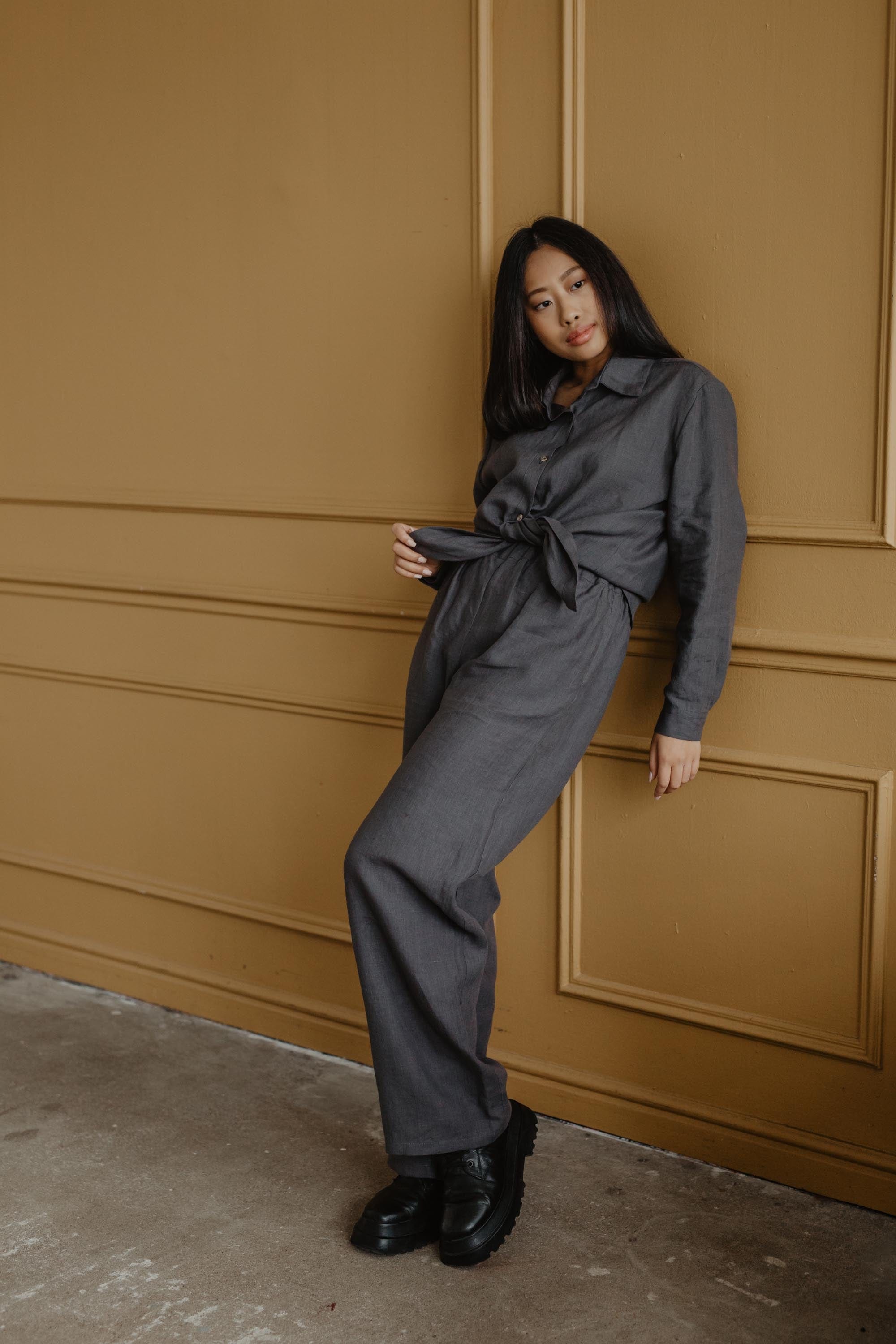 Woman Leaning On Wall Wearing A Dark Linen Casual Shirt And Grey Linen Pants By AmourLinen