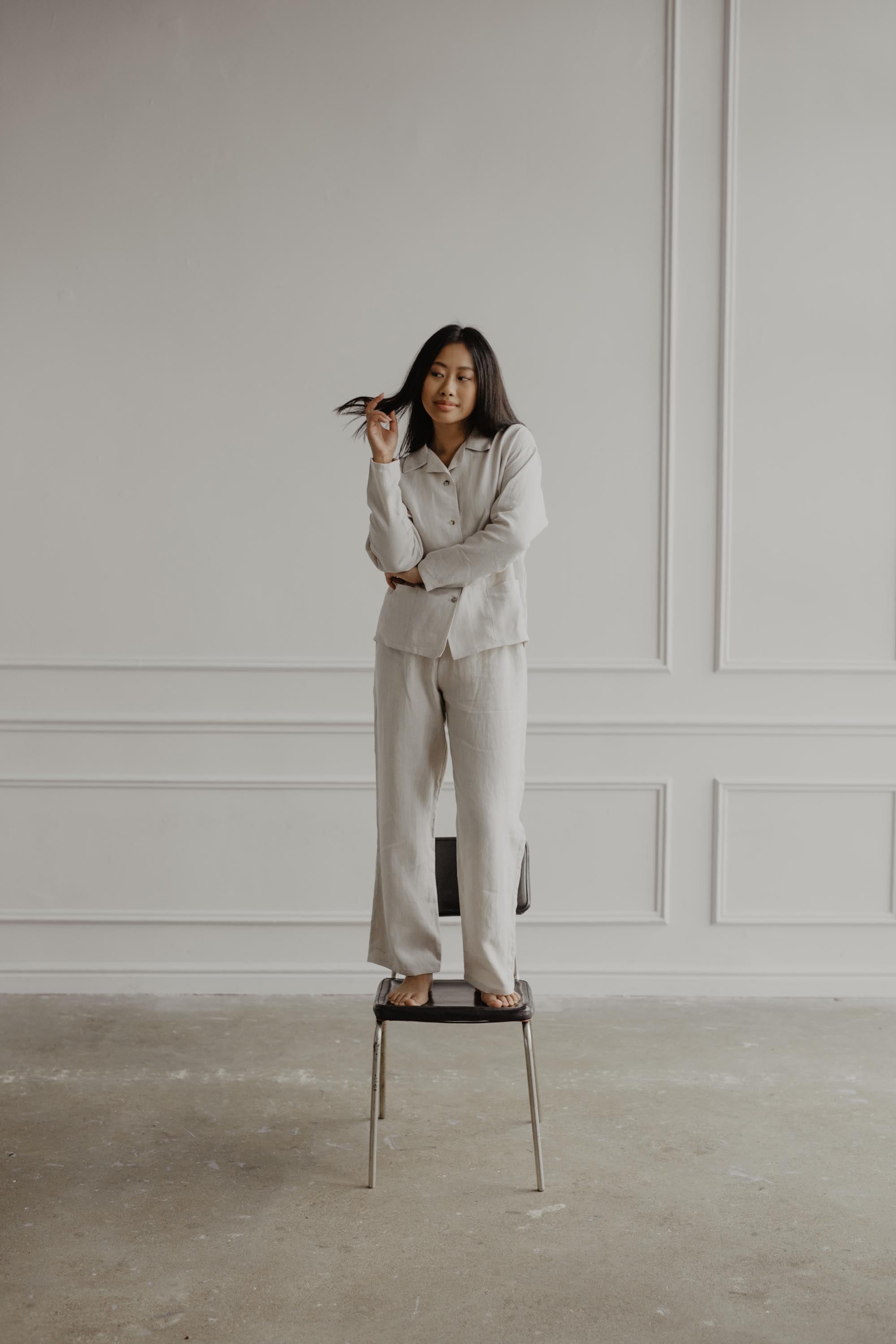 Woman Standing On Chair Wearing A White LInen Pajama Set By Amourlinen