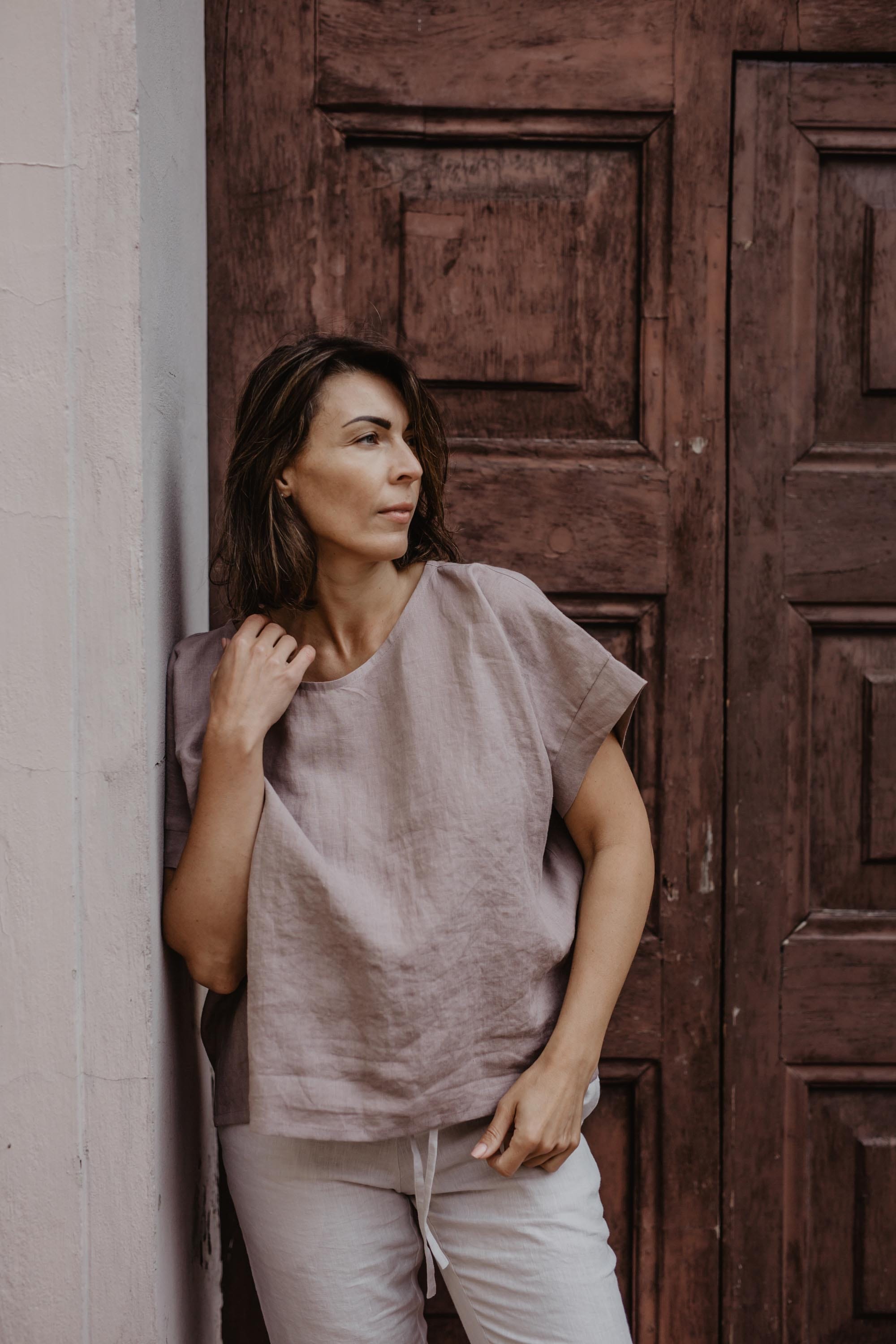 Woman Leaning Against A Wall Wearing A Dusty Rose Linen Top By Amourlinen