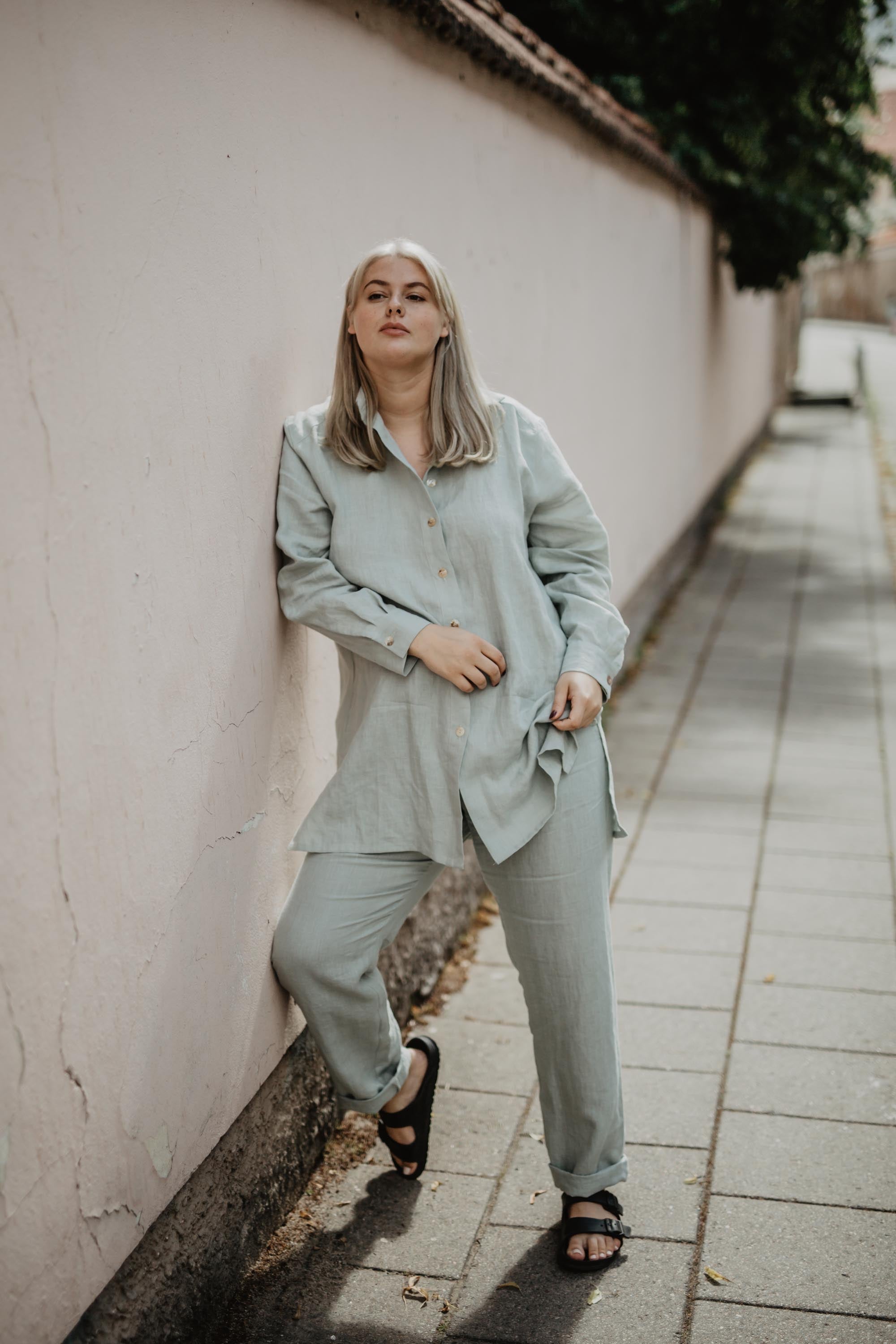 Woman Leaning On Wall  Wearing Sage Green Linen Suit Set By AmourLInen
