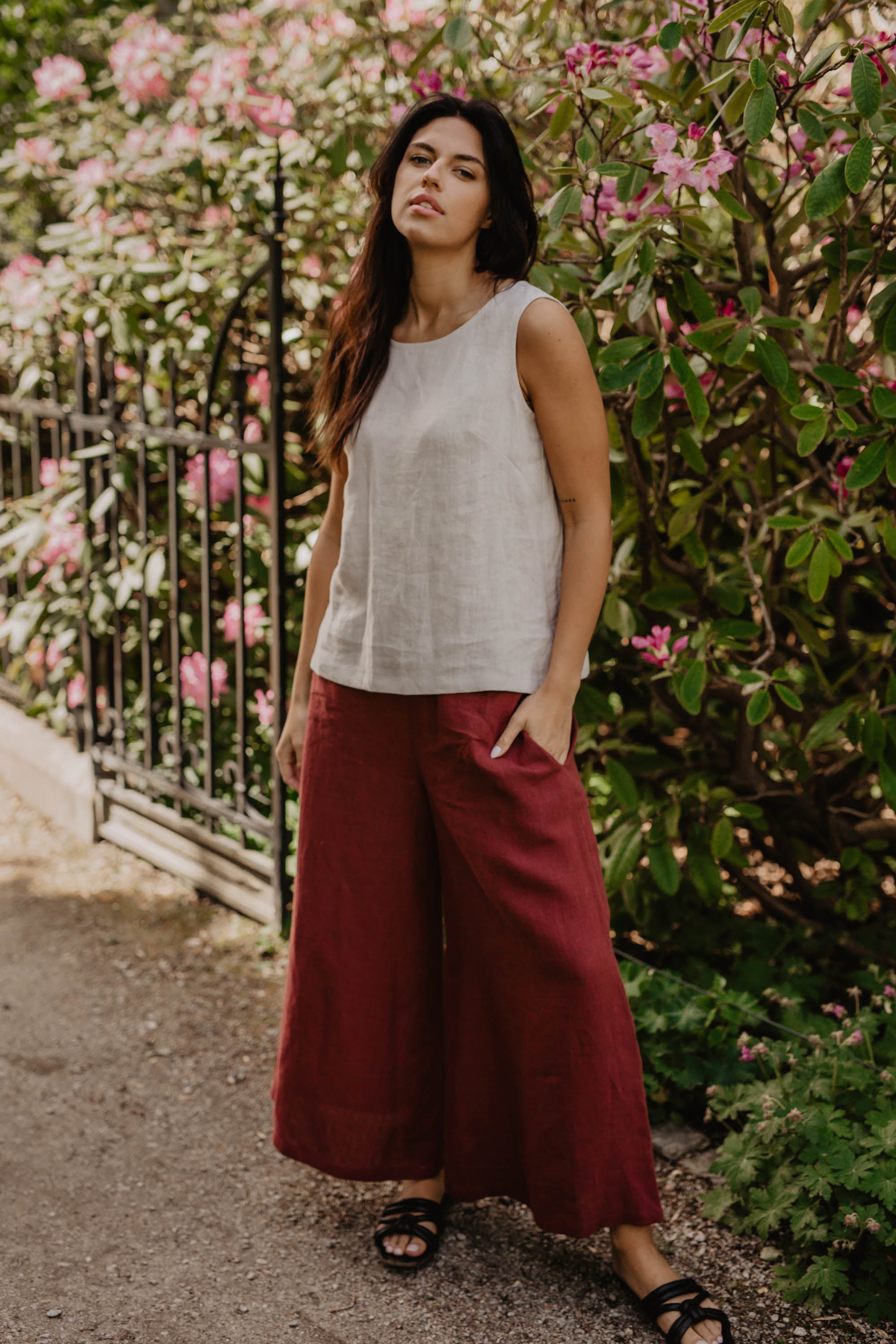 Woman With White Linen Top And Red Linen Pants Posing In Flowery Garden