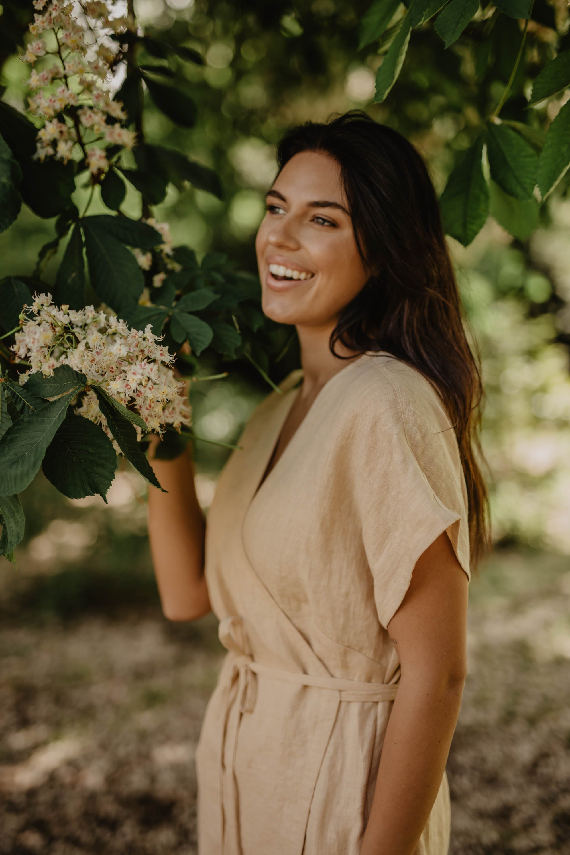 Close Up Of Women In Mustard Linen Dress Next To A Blossoming Tree
