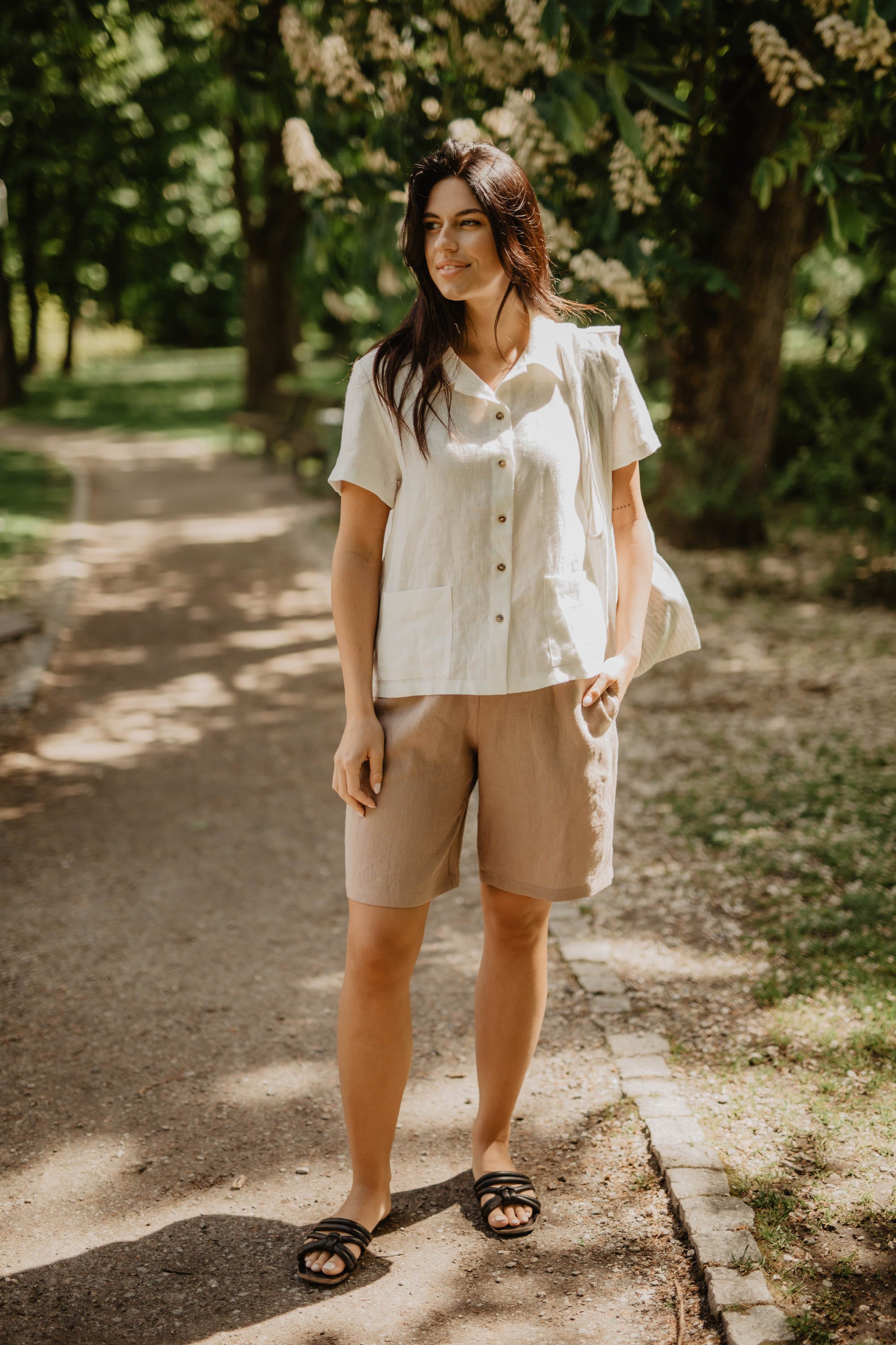 Linen Standing In Park Wearing A white Linen Shirt and Dusty Rose Linen Shorts