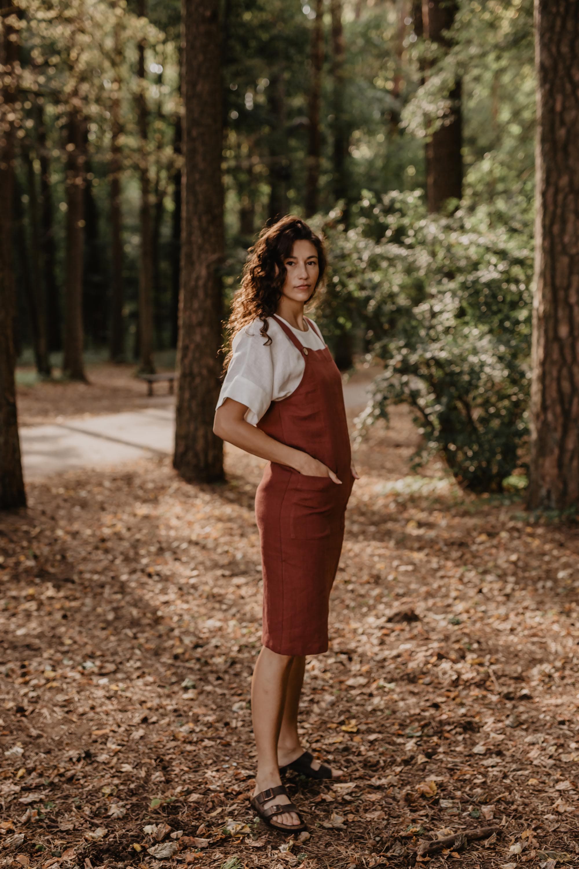 Side Of Women Wearing A Red Linen Apron Dress With White Top