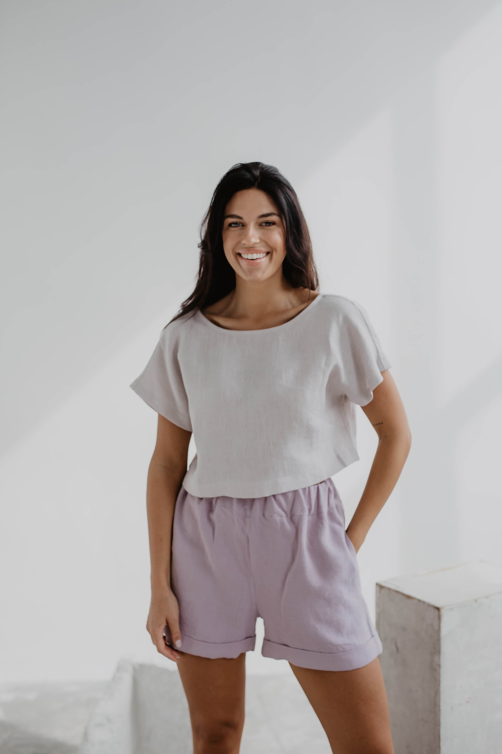Woman Facing Forward Wearing A White Linen Crop Top and Pink Linen Shorts In Gallery