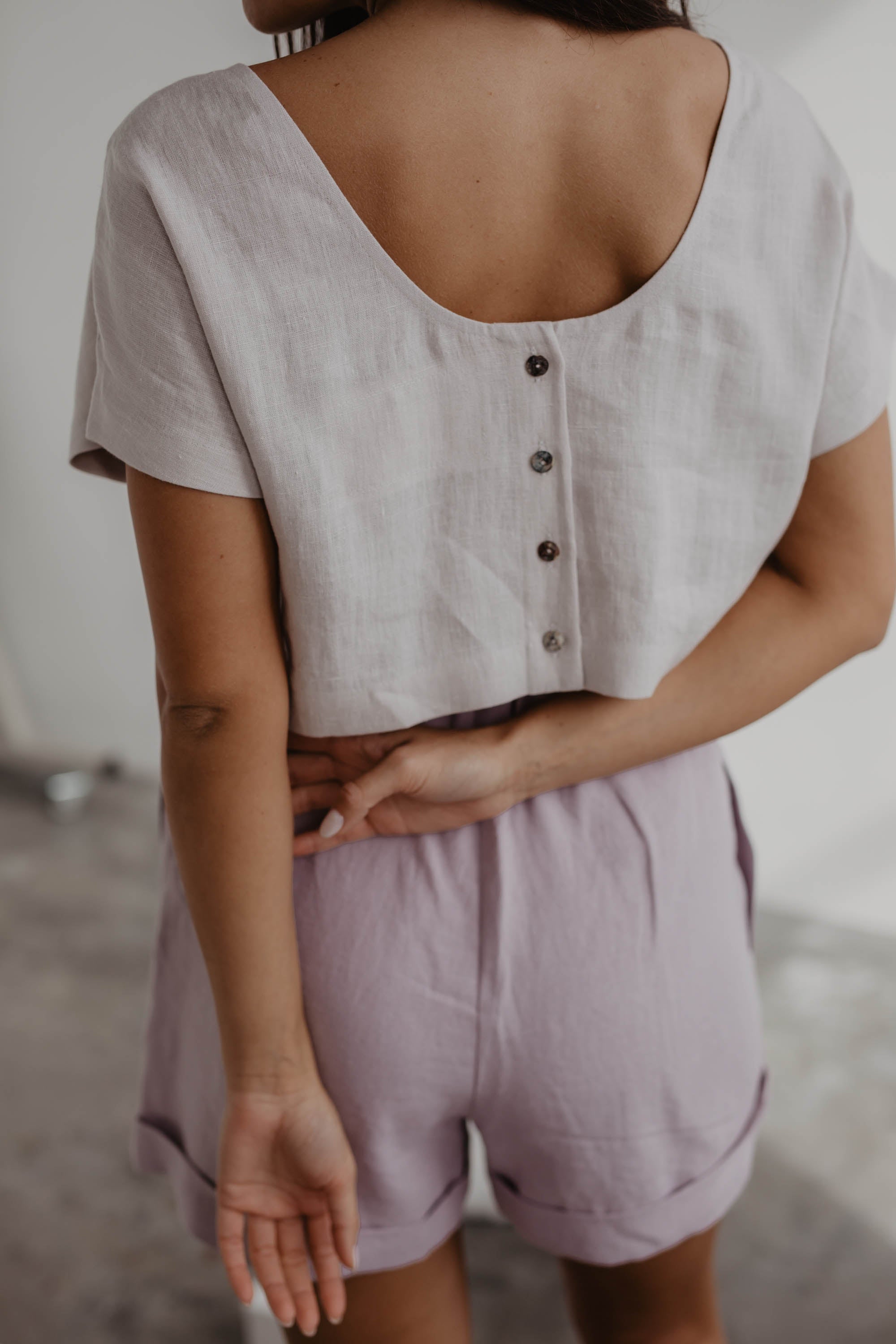 Close Up Of Woman Facing Back Wearing A White Linen Crop Top With Buttons And Pink Linen Shorts