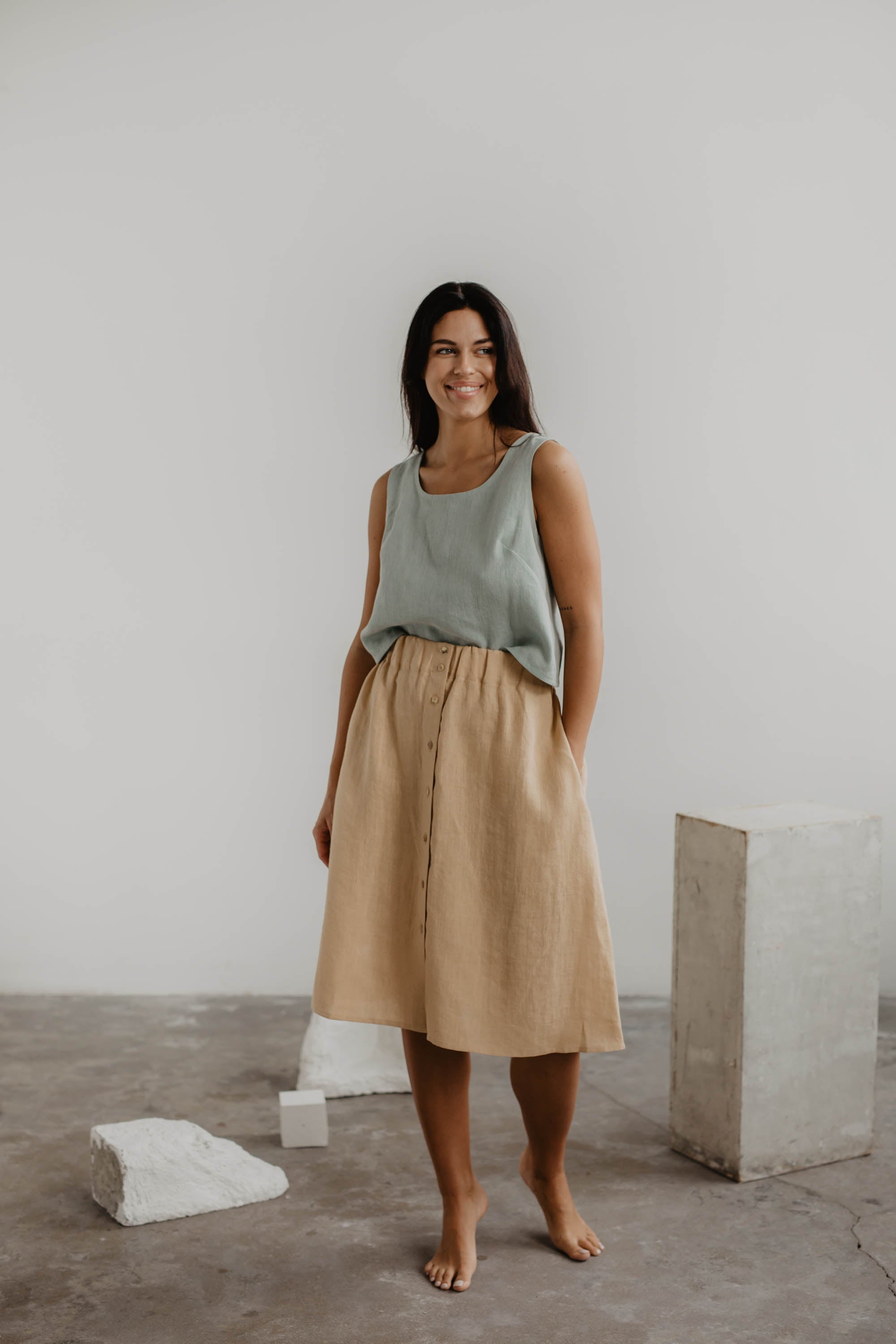 Woman Wearing A Sage Green Linen Pinafore Top and A Mustard Linen Long Skirt In A Gallery