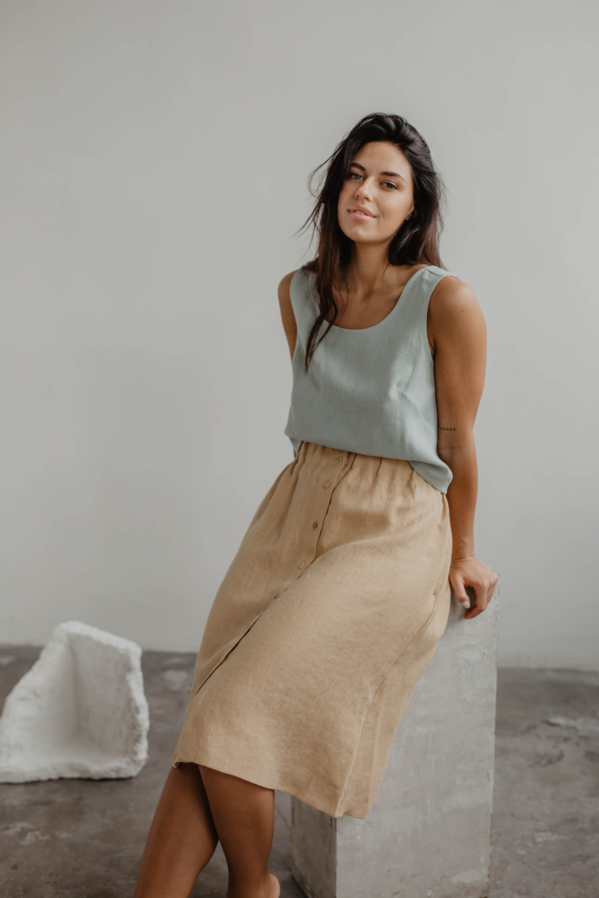 Woman Sitting On Concrete Block Wearing A Mustard Color Linen Skirt With buttons By AmourLinen