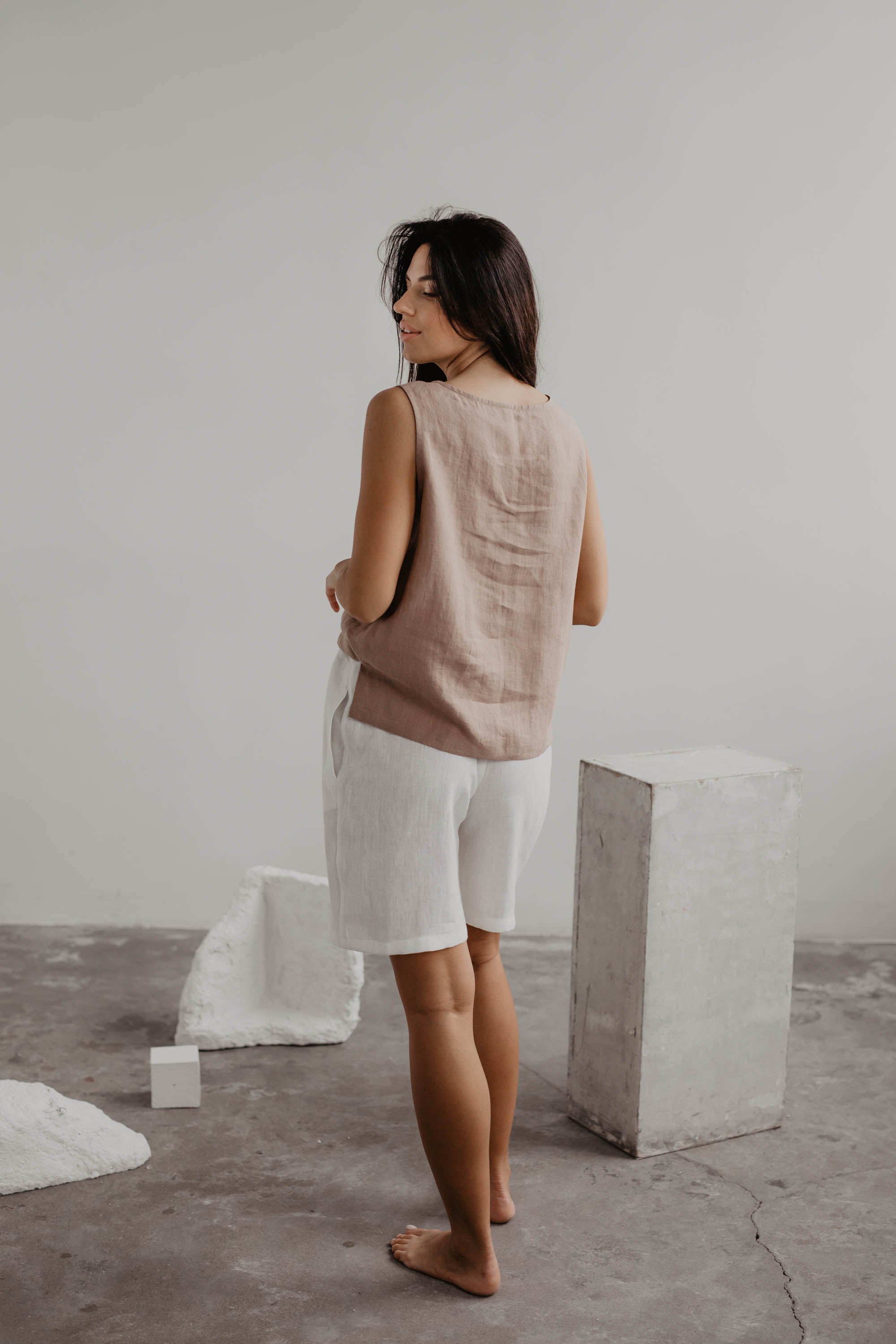 Back Of Woman Wearing A Dusty Rose Linen Top And White Linen Shorts