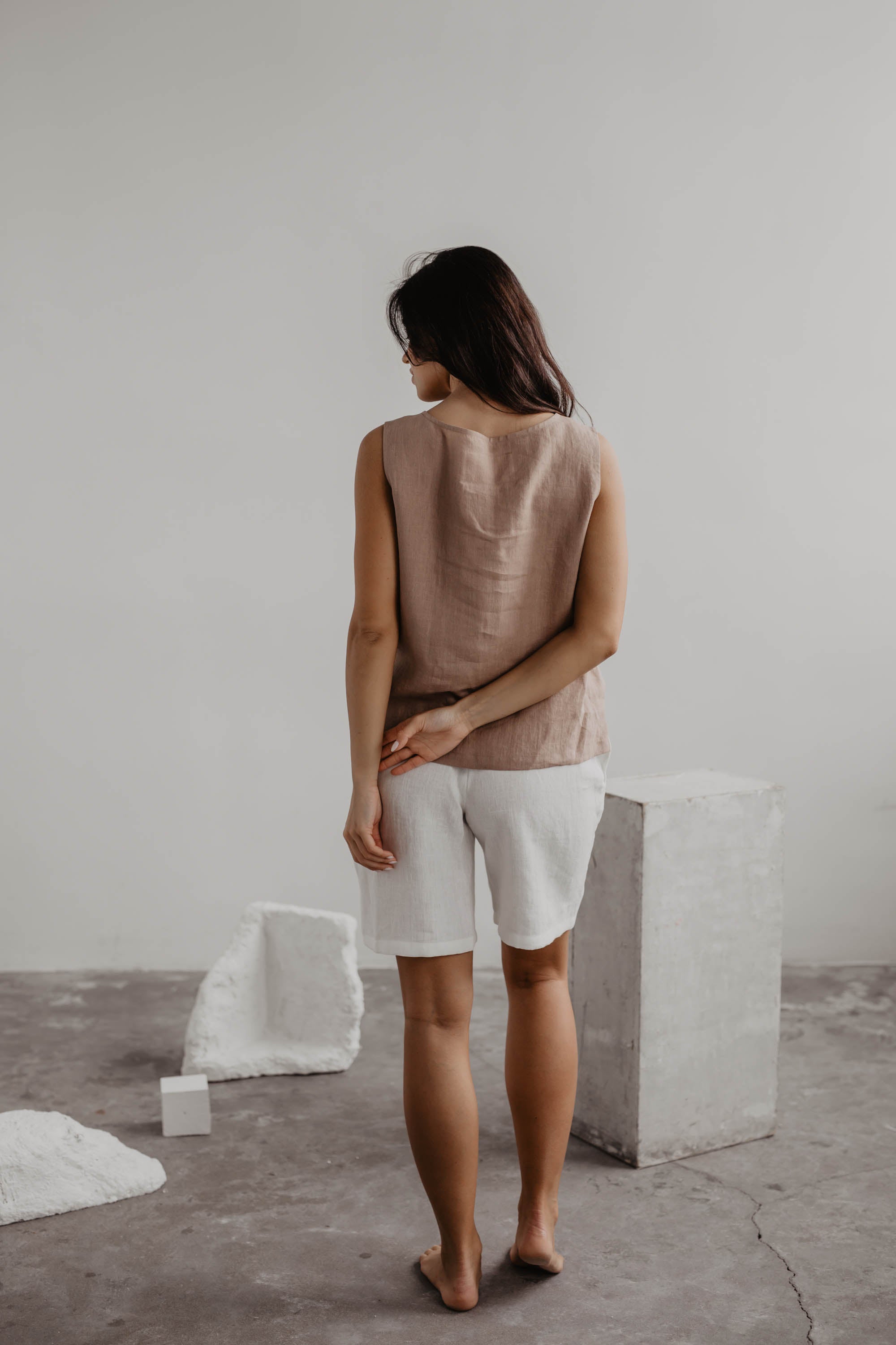 Back Of Woman Wearing A Dusty Rose LInen Top And White Linen Shorts In A Gallery