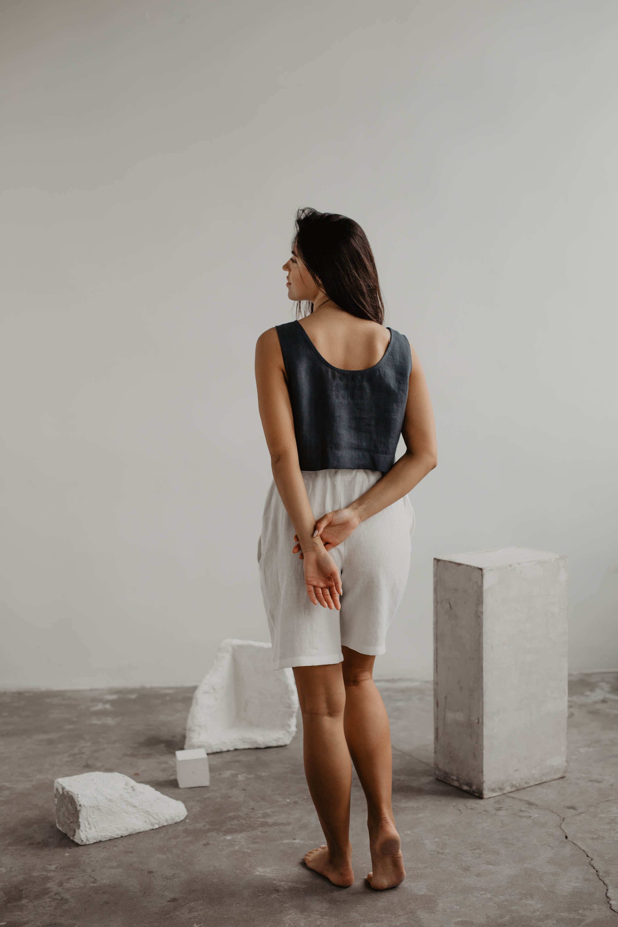 Woman Facing Back Wearing A Dark linen Crop Top And White Linen Shorts In A Gallery