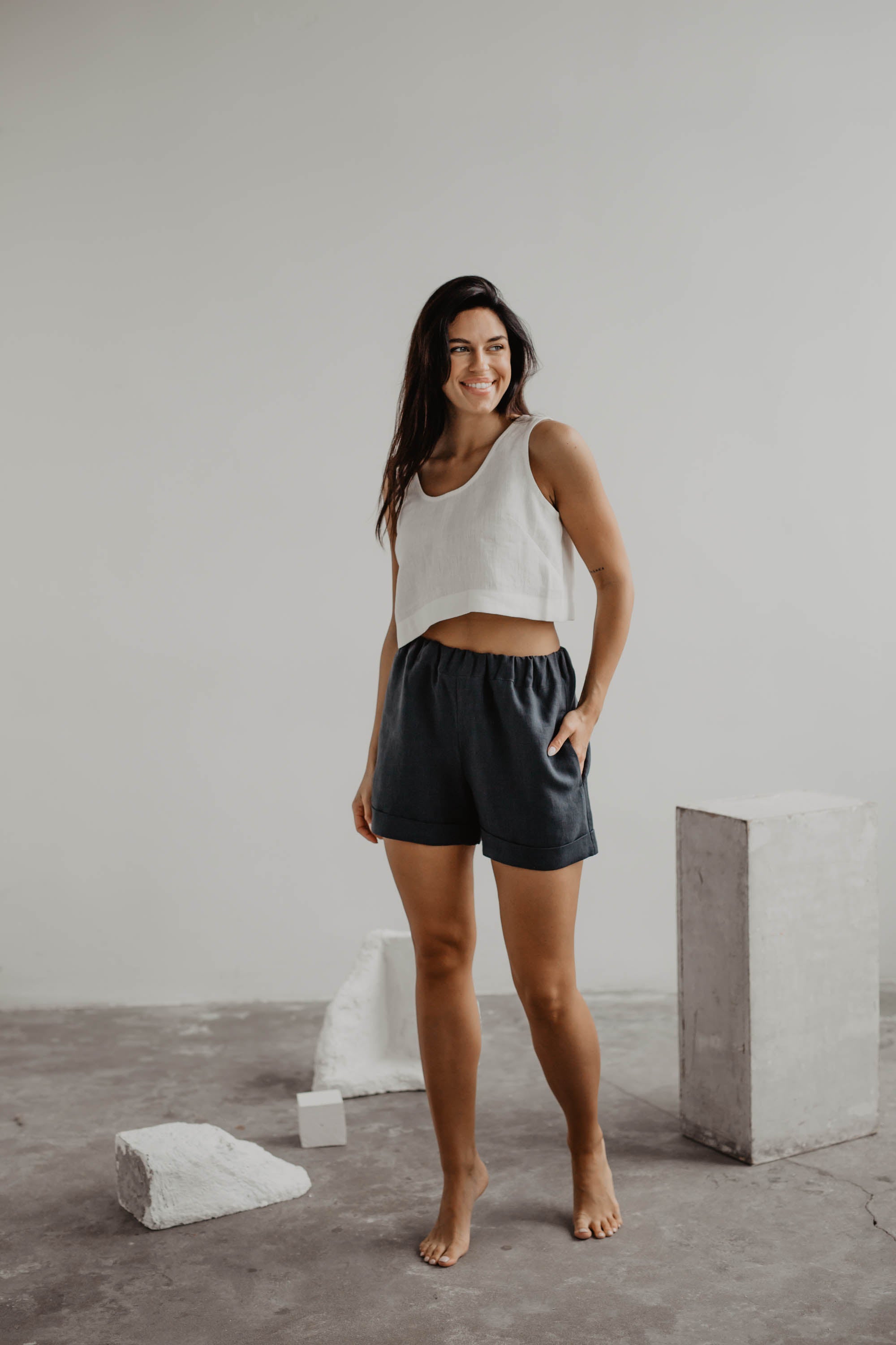 Woman Wearing A White Linen Crop Top And Dark Linen Shorts In Gallery