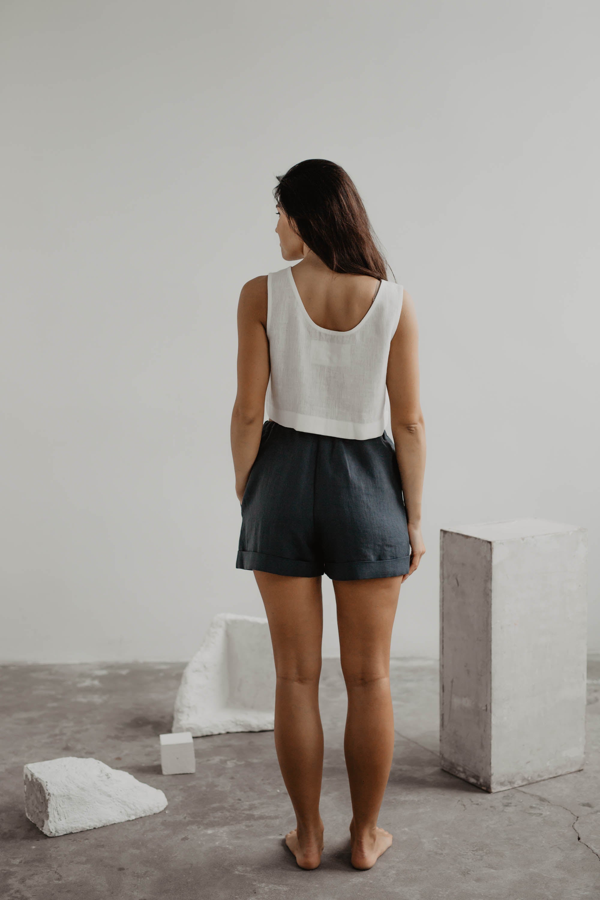 Woman Facing Back Wearing White Linen Crop Top And Charcoal Linen Shorts In A Gallery