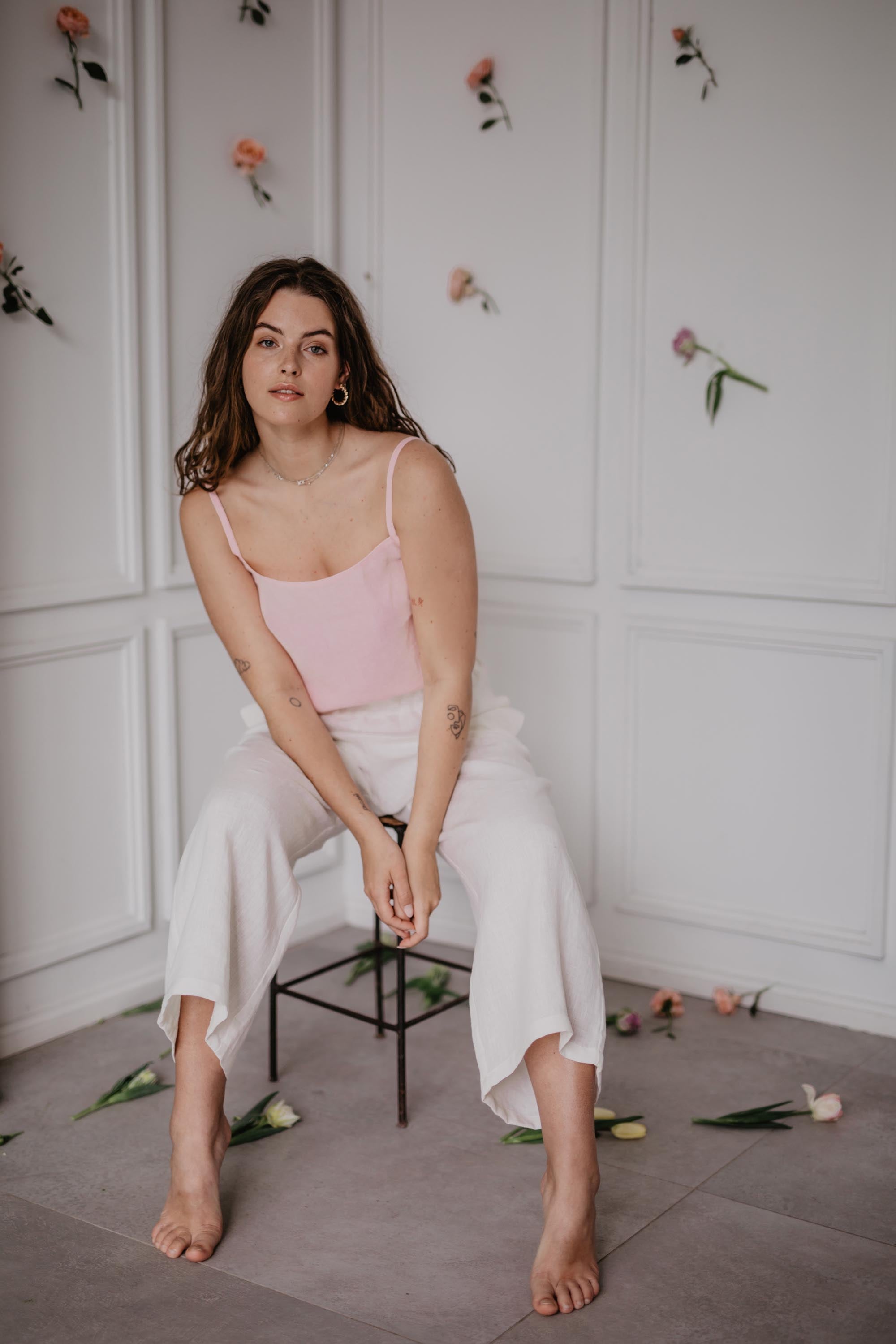 Woman Sitting In A Flowery Room Wearing A Pink Linen Top and Whitte Linen Pants By Amourlinen