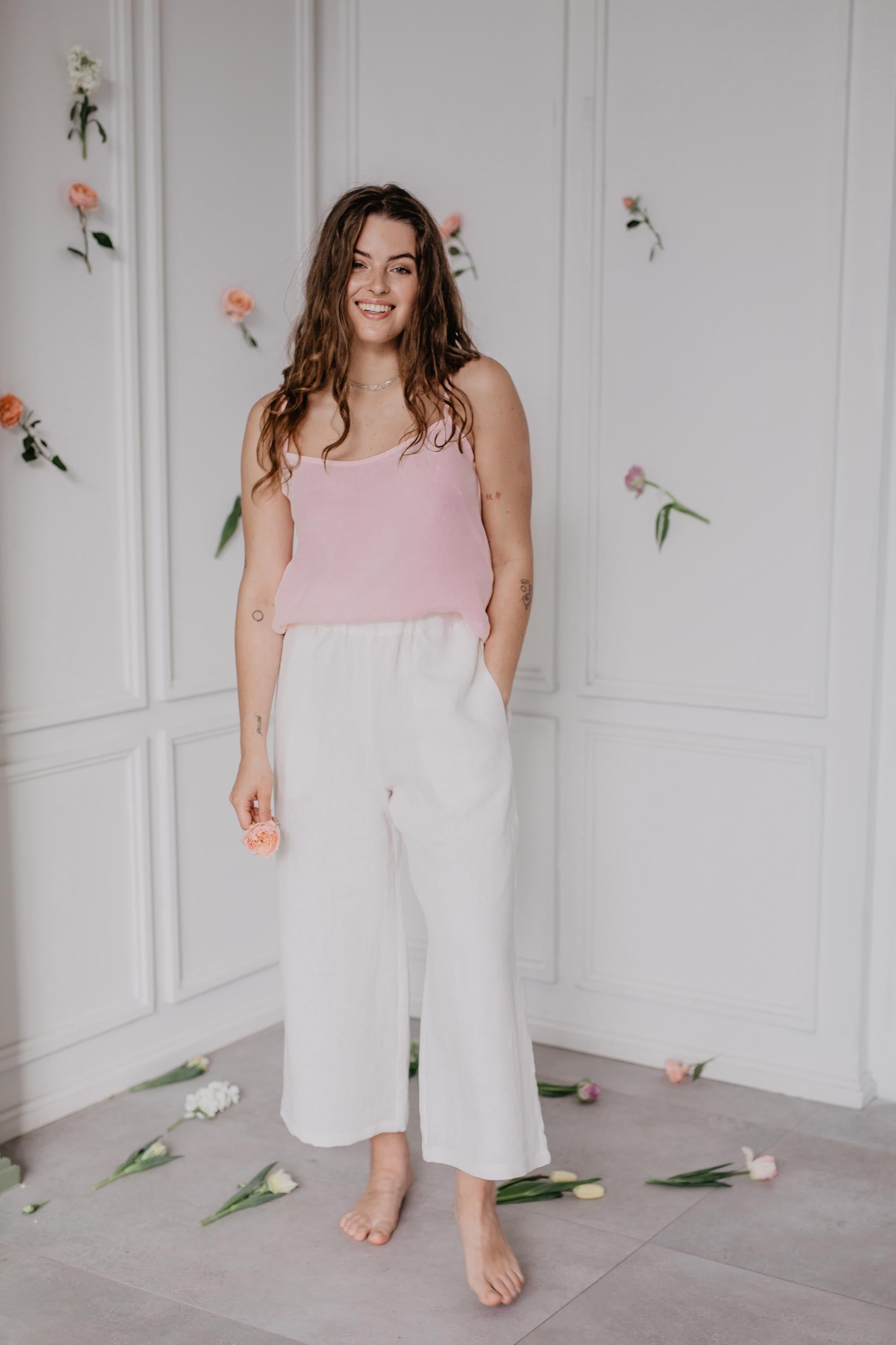 Woman In A Flowry Room Wearing A Pink Linen Top and Whitte Linen Pants By Amourlinen