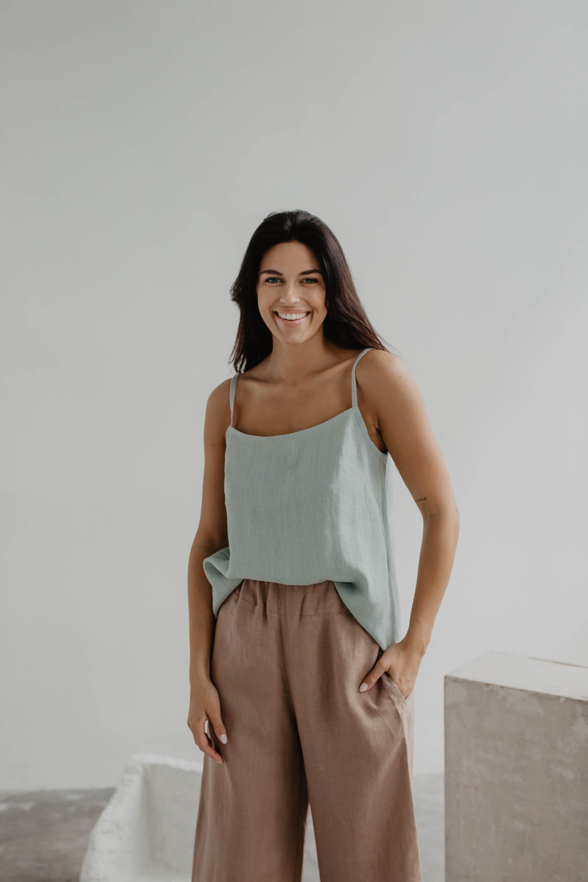 Woman In A Gallery Wearing A Sage Green Linen Top and Dusty Rose Linen Pants By Amourlinen