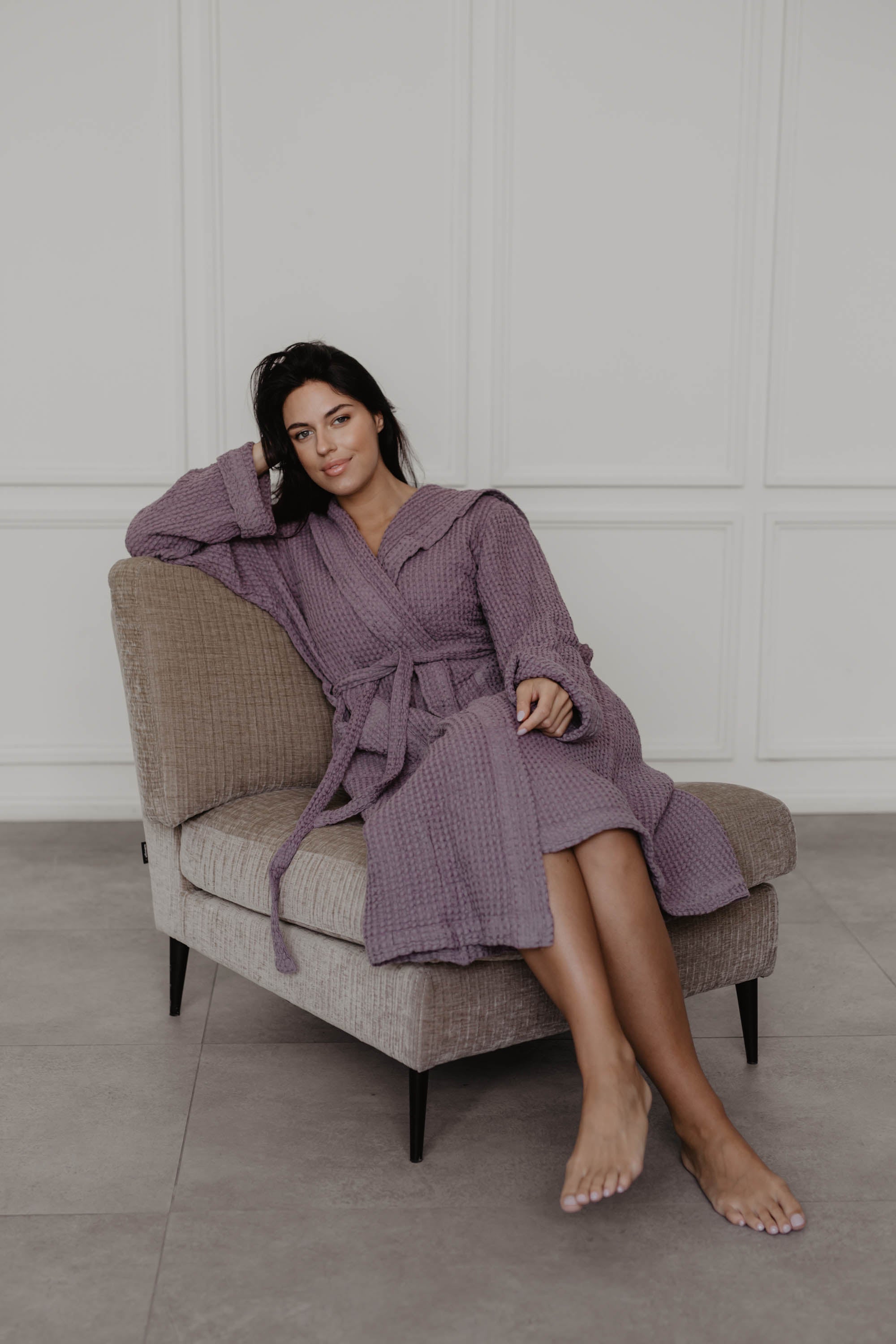 Woman Sitting On Sofa Wearing A Dusty Lavender Linen Waffle Style Bathrobe