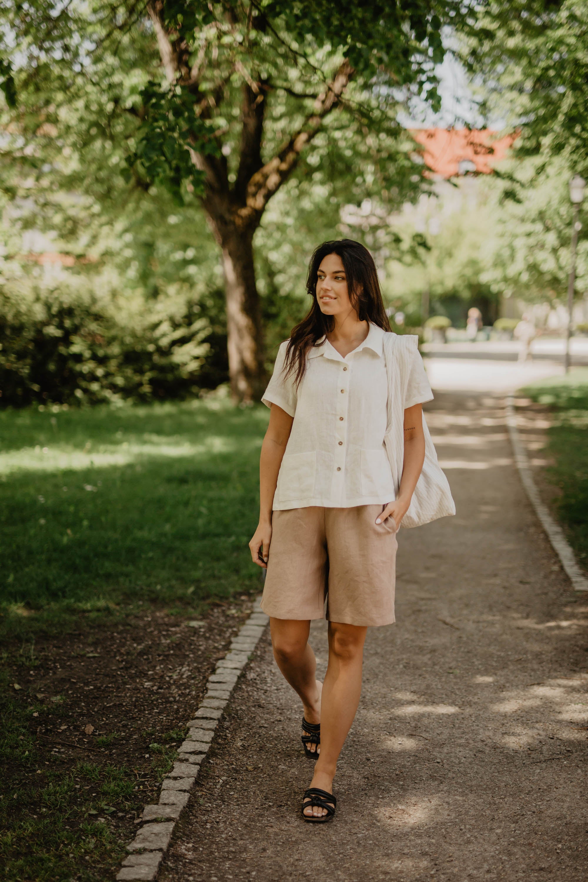 Woman In Park Walking In Cream Color Long Linen Shorts and A Short Sleeved White Linen Shirt