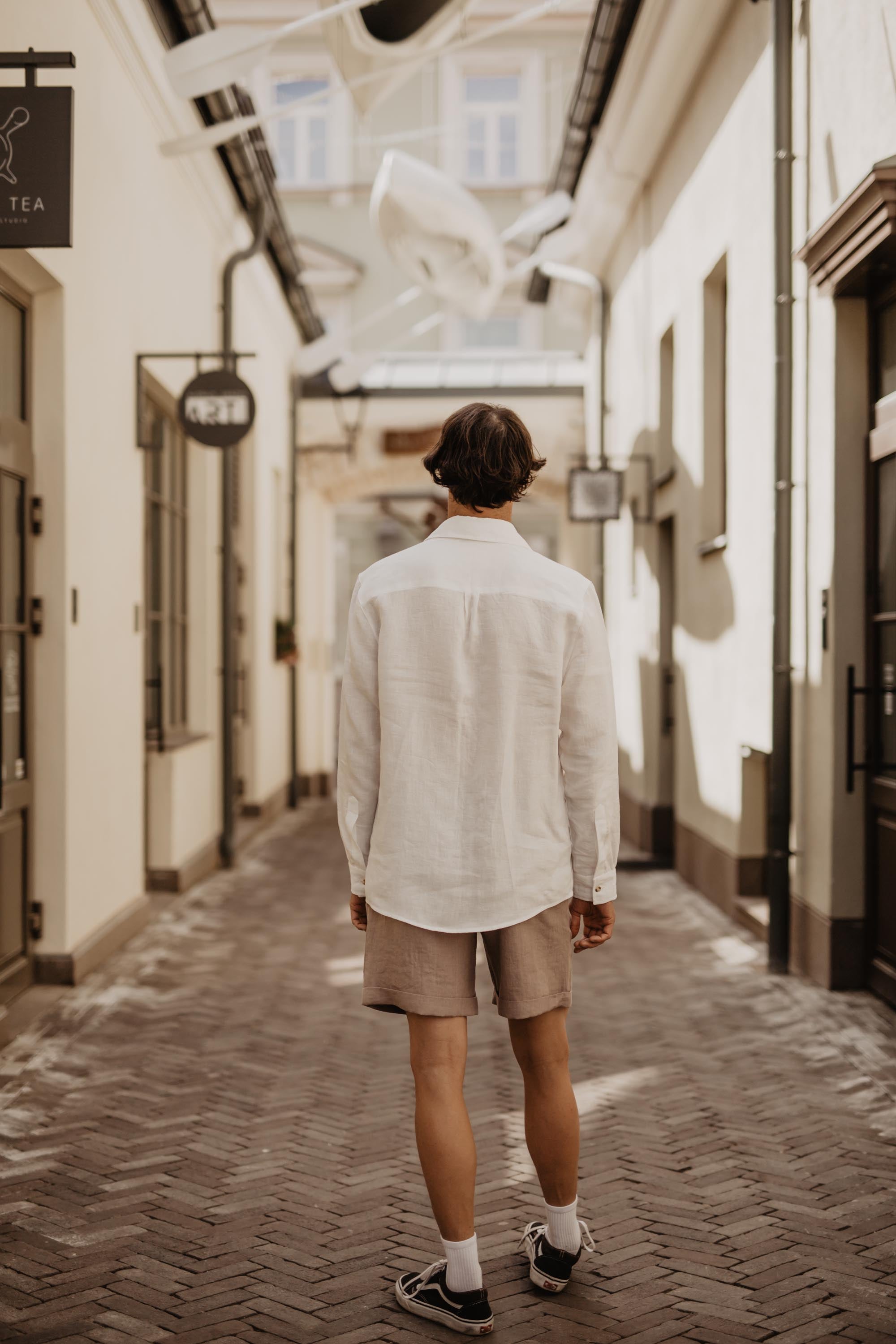 Man Wearing White Linen Shirt And Light Shorts Looking Down The Street