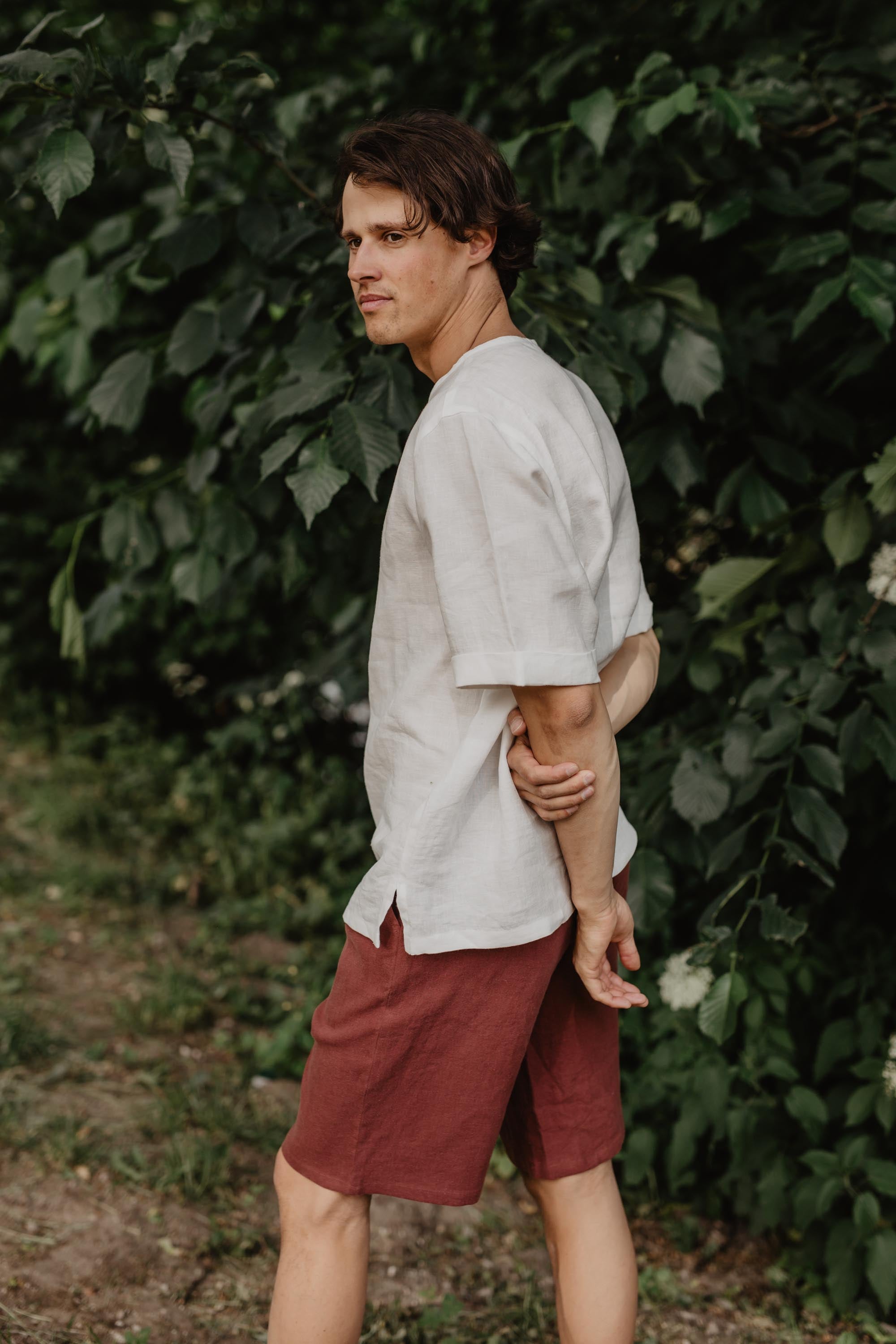 Man In Nature Looking To The Side Wearing A White Linen Top And Terracotta Shorts