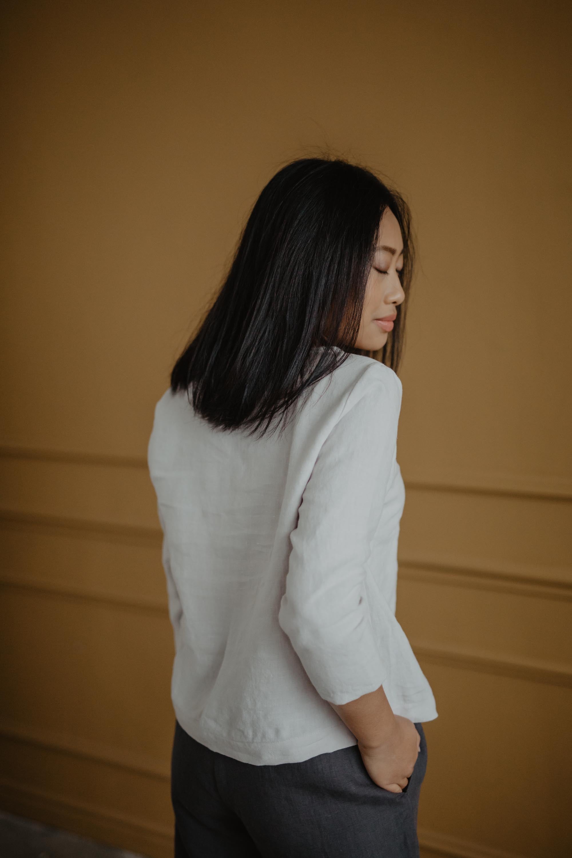 Woman Looking OVer Shoulder Wearing  A White Linen Top And Grey Linen Pants