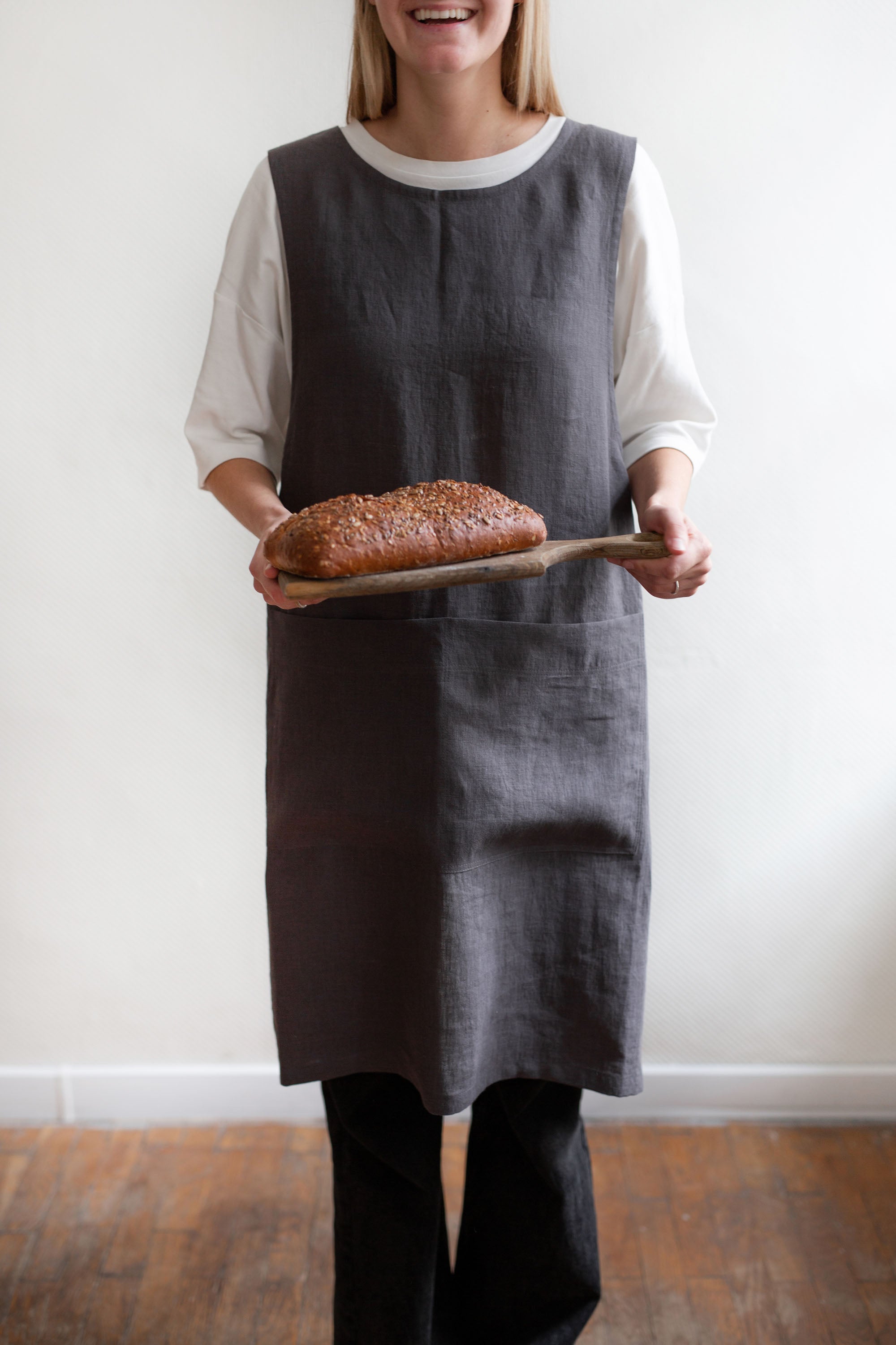 Woman Holding a Bread Loaf Wearing Pinafore Linen Apron In Charcoal By AmourlInen