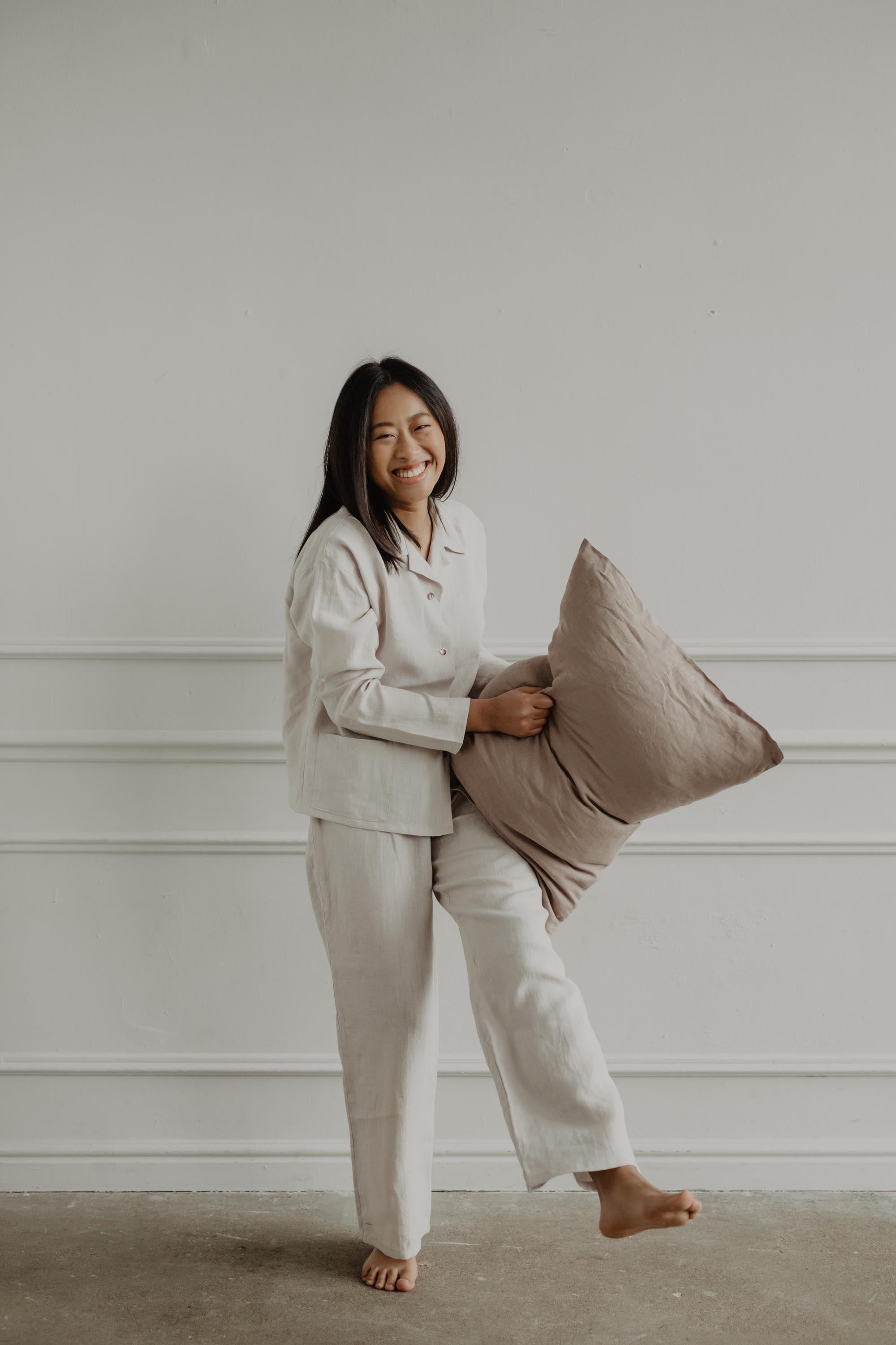 Woman Laughing and Holding a Pillow Wearing A White Linen Pajama Set By AmourLinen