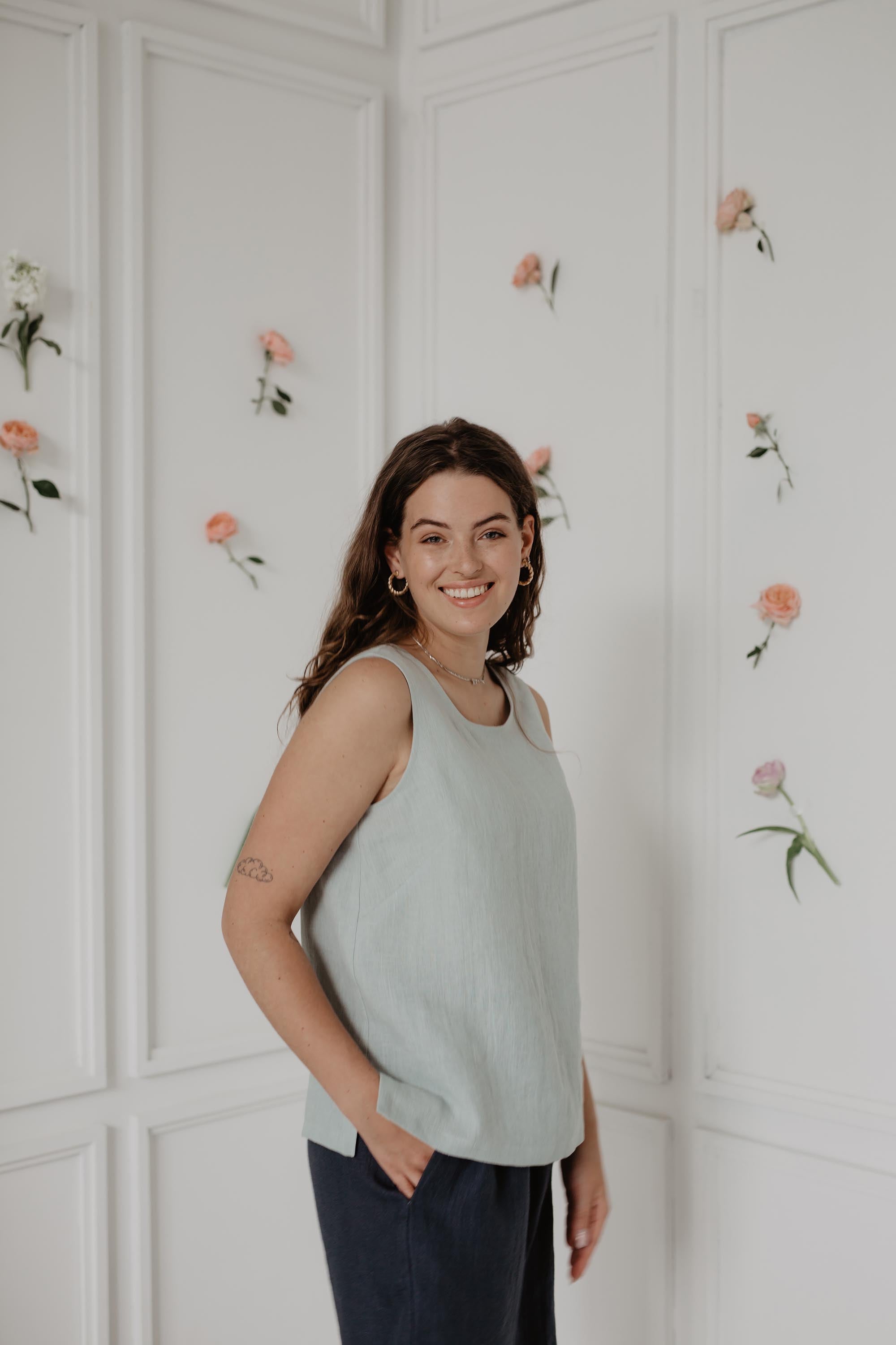 Woman Wearing A Sage Green Linen Top and Navy Blue Linen Shorts In White Flowery Room
