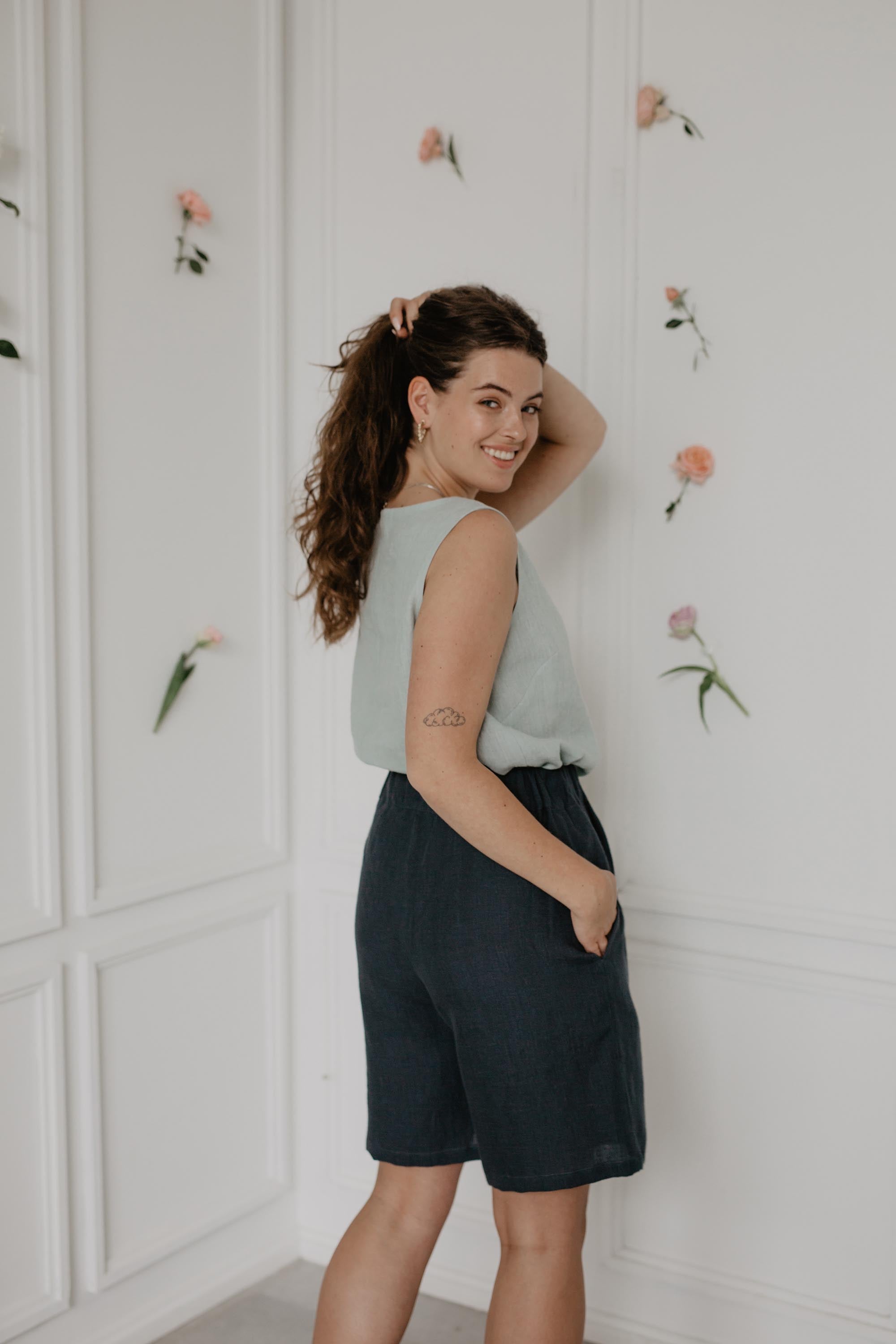 Back Of Woman Wearing Dark Long Linen Short and A Sage Green Top in A Flowery Room