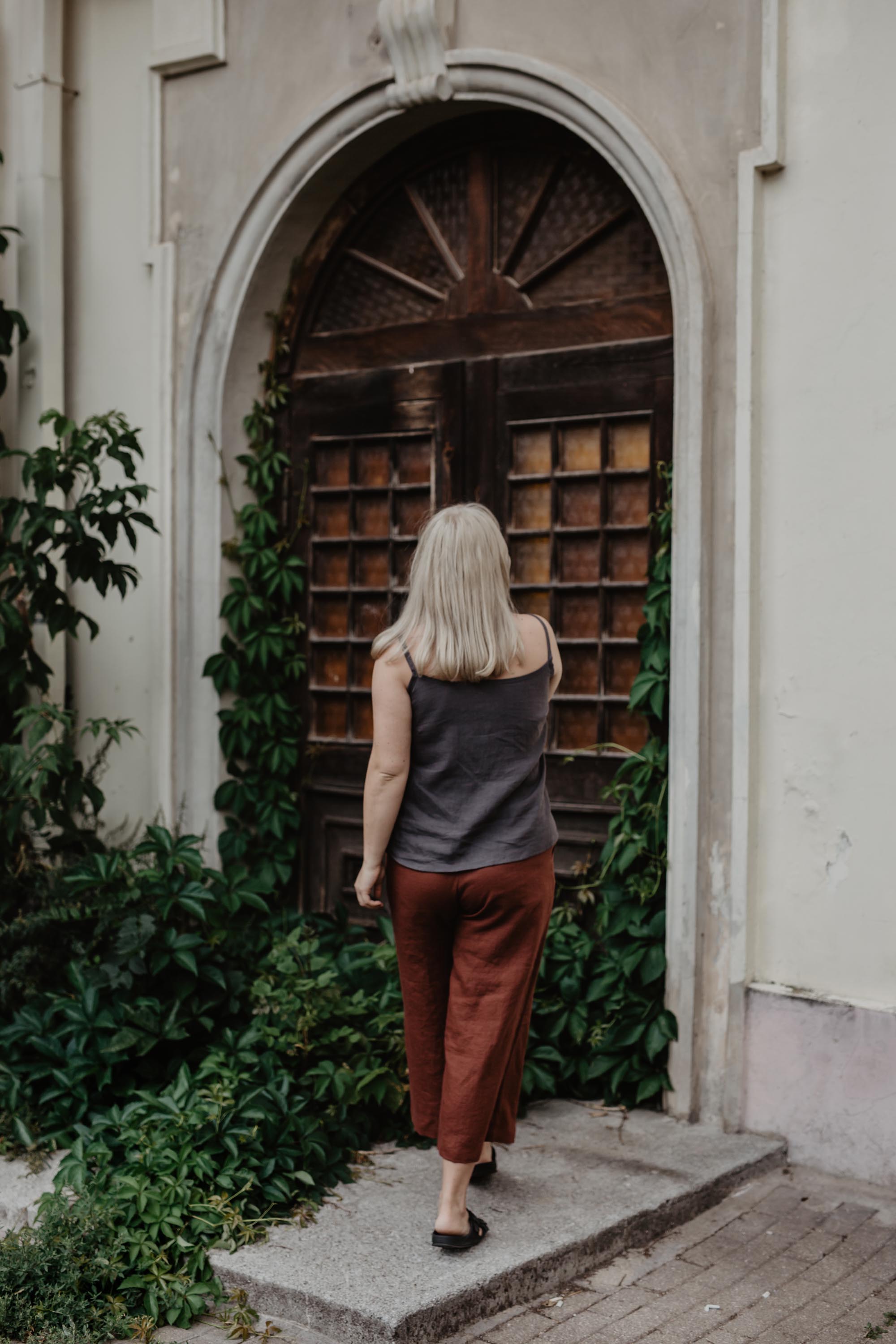 Woman In Facing Back Wearing Terracotta Linen Pants and Dark Linen Top By Amourlinen