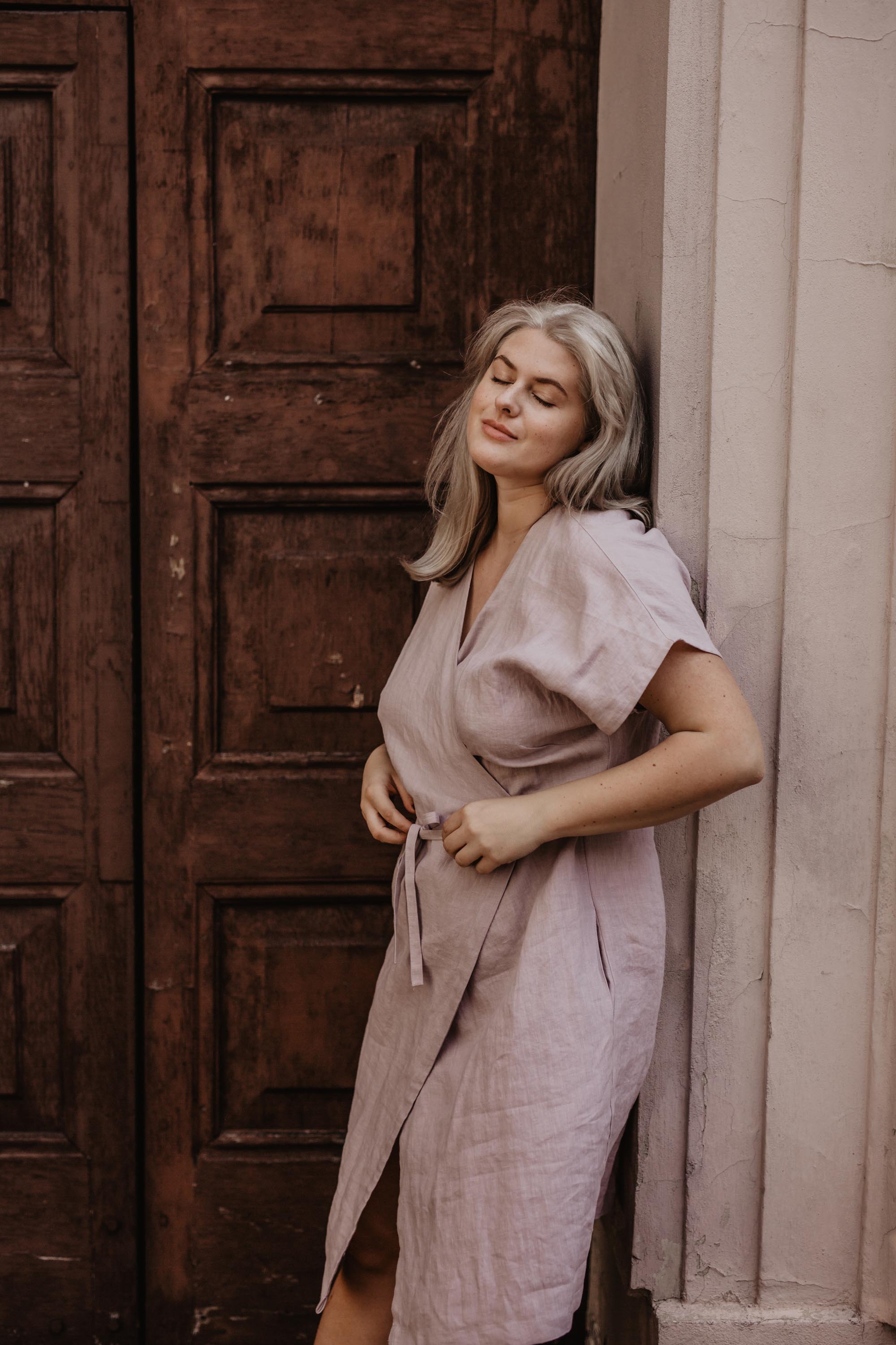 Woman Next to a door wearing a Dusty Rose lInen wrap dress by Amourlinen