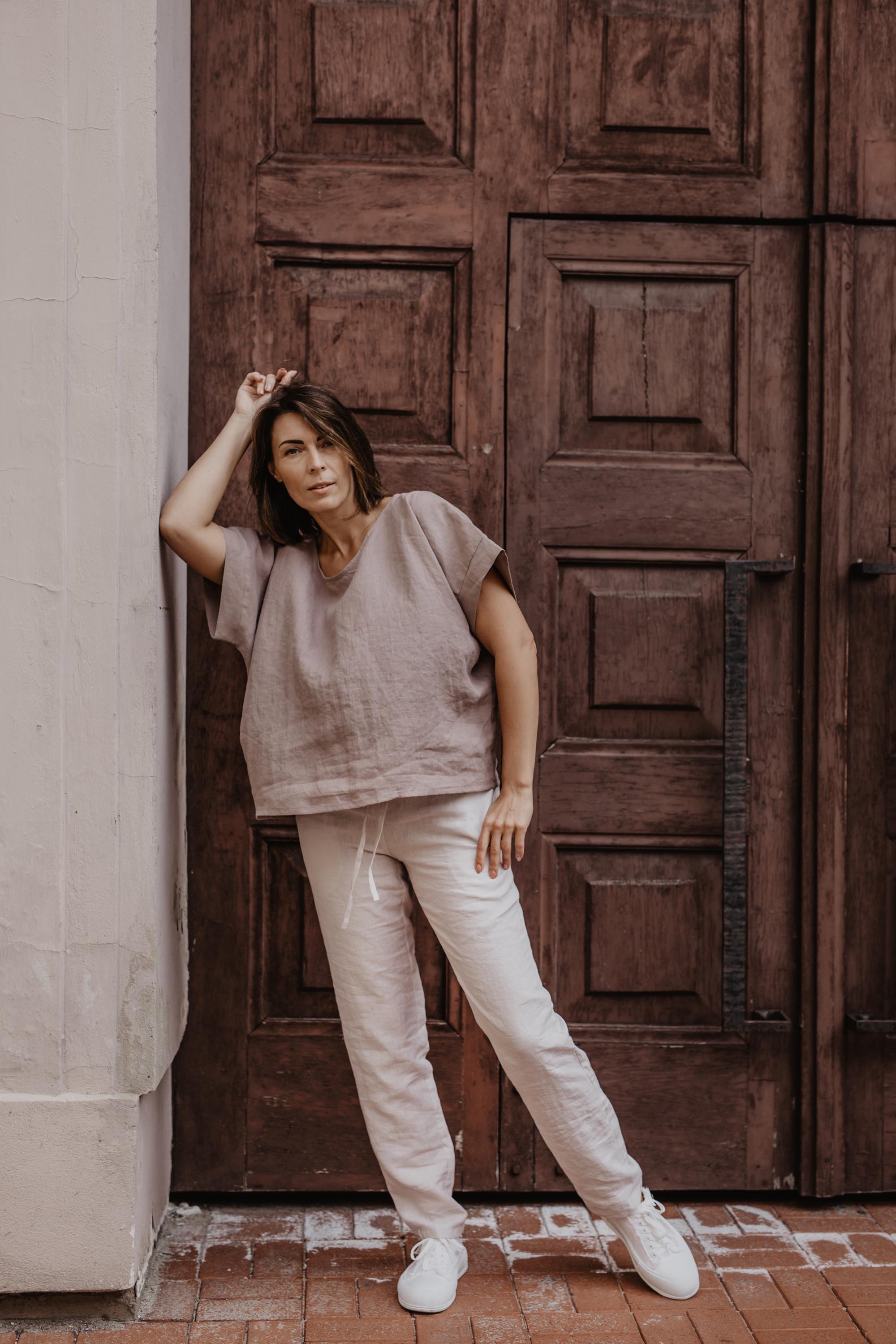 Woman Leaning Against A Wall Wearing A White Linen Pants and Dusty Rose Linen Shirt By Amourlinen