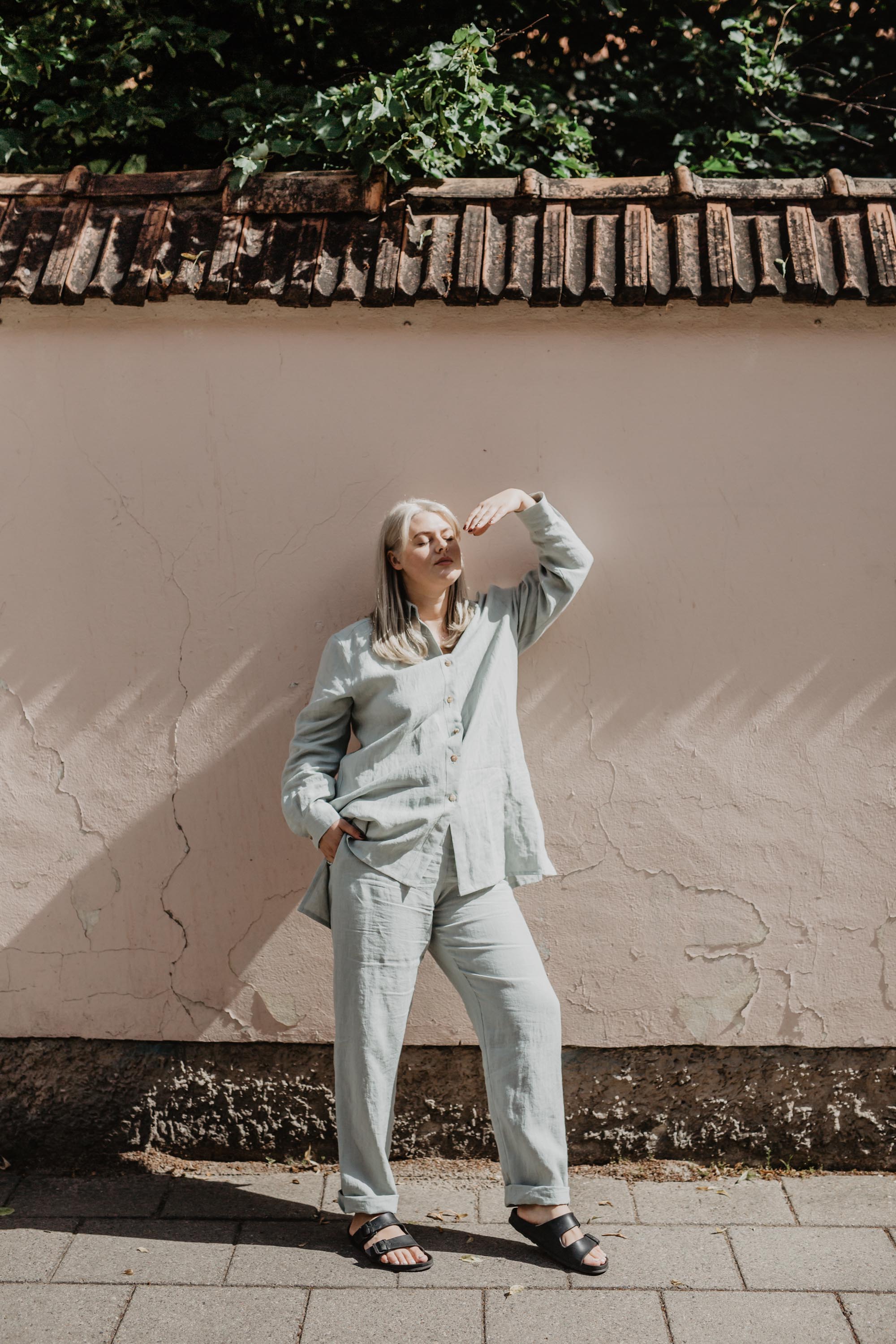 Woman Posing In Front of A Rustic Wall Wearing Sage Green Linen Suit Set By AmourLInen